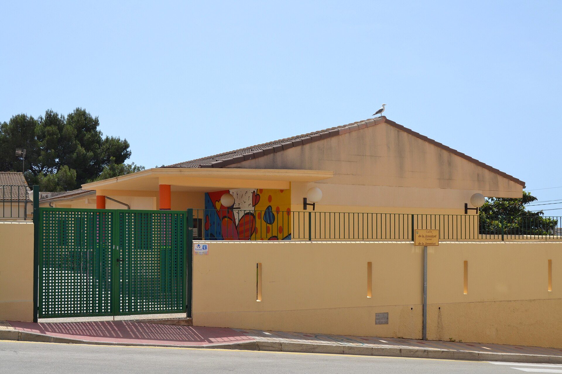 A single-story house with a colorful mural, green gate, and a clear blue sky view.