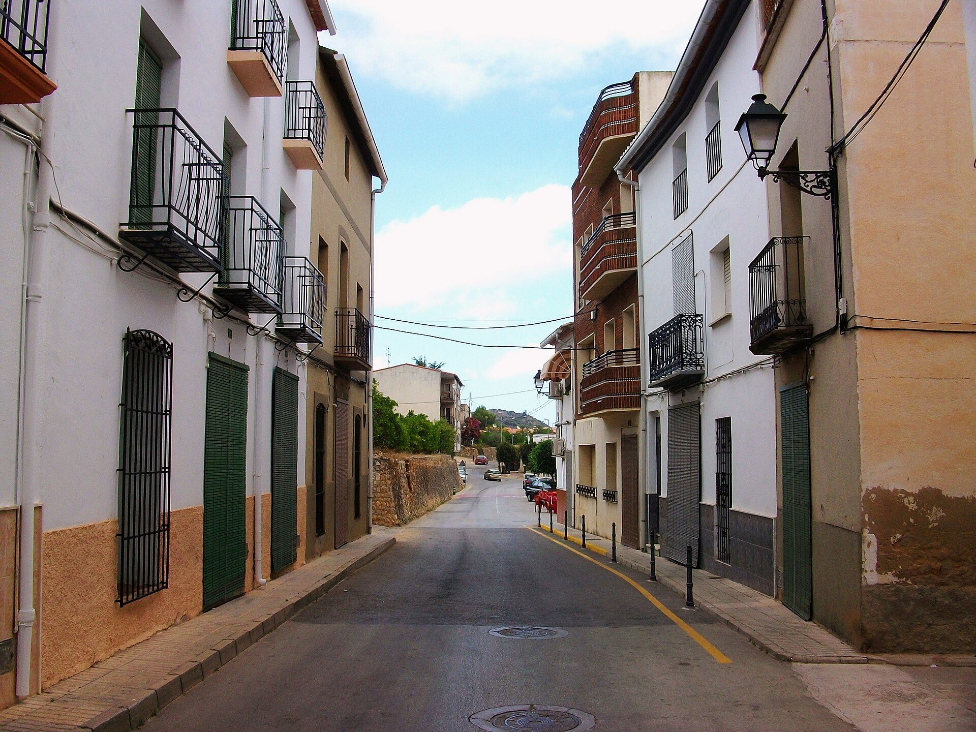 Narrow street with multi-story buildings, balconies, and a clear sky.