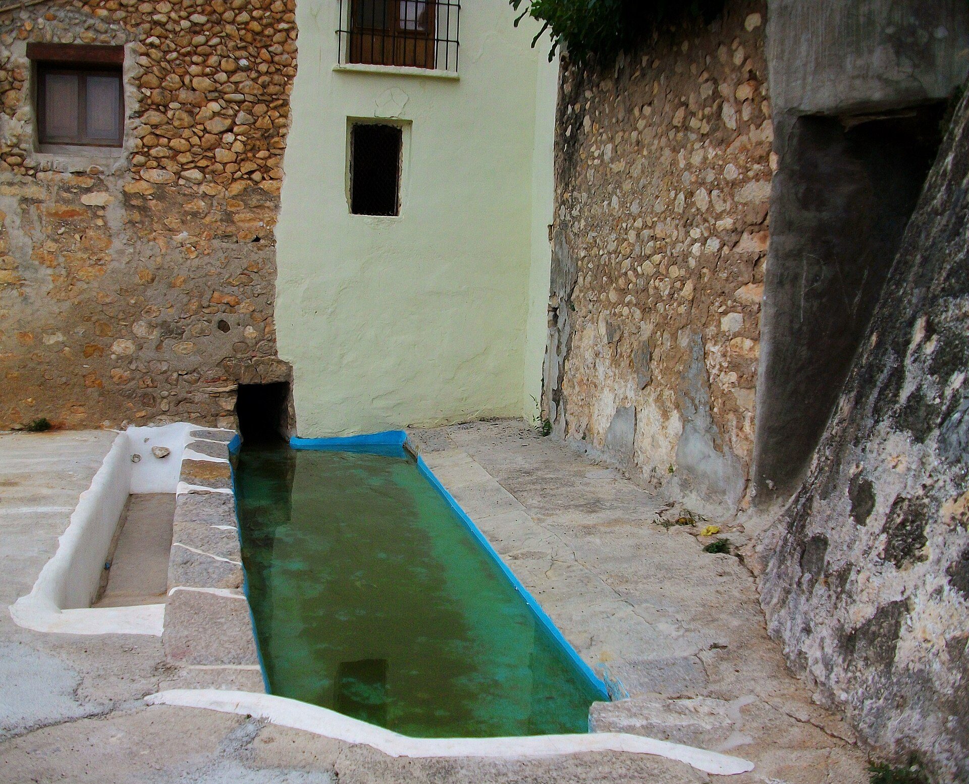 Outdoor pool with stone walls, small windows, and a rustic ambiance.