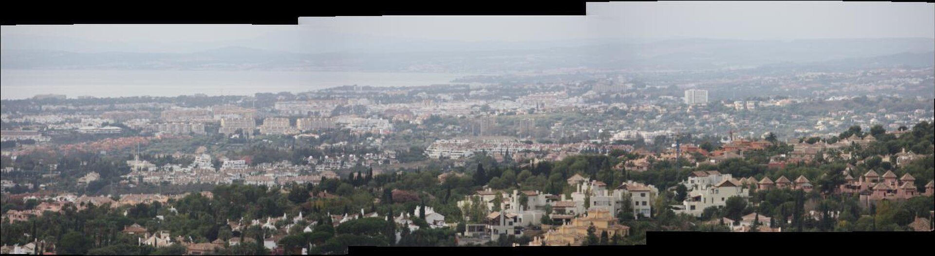 Spacious living room with panoramic city and sea views, modern furnishings, large windows.