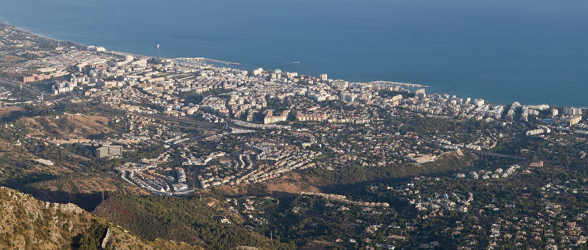 Aerial view of a coastal city with ocean and mountainous landscape.