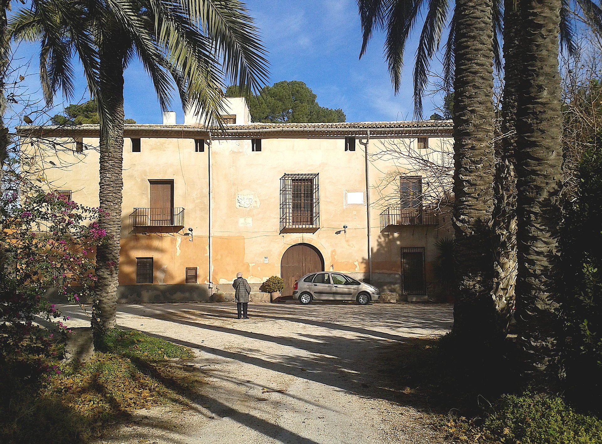 Two-story villa with a courtyard, palm trees, and a parked car.