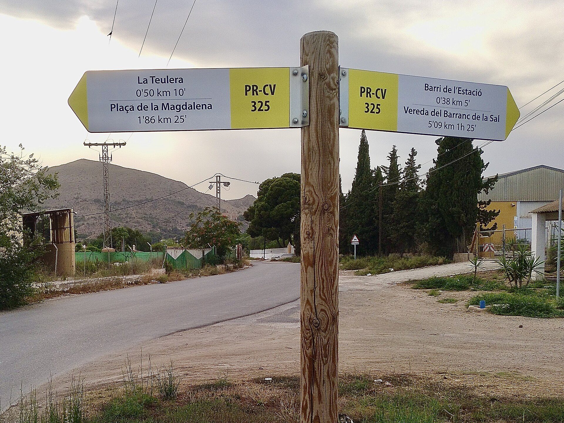 A wooden signpost with directions to La Teulera and Barri de l'Estel, with a mountainous landscape in the background.