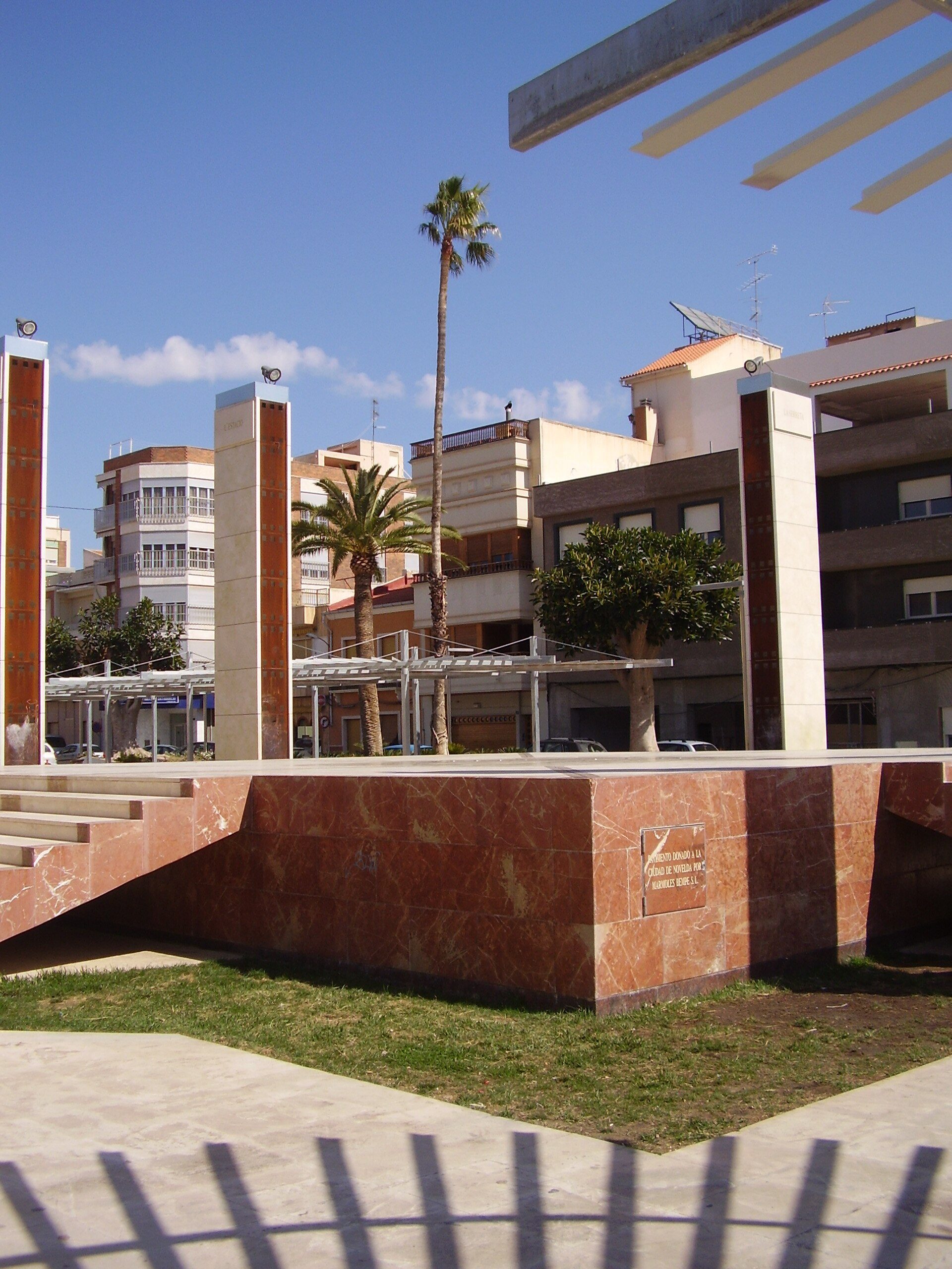 Alt text: Outdoor area with palm trees, modern building, and clear blue sky.