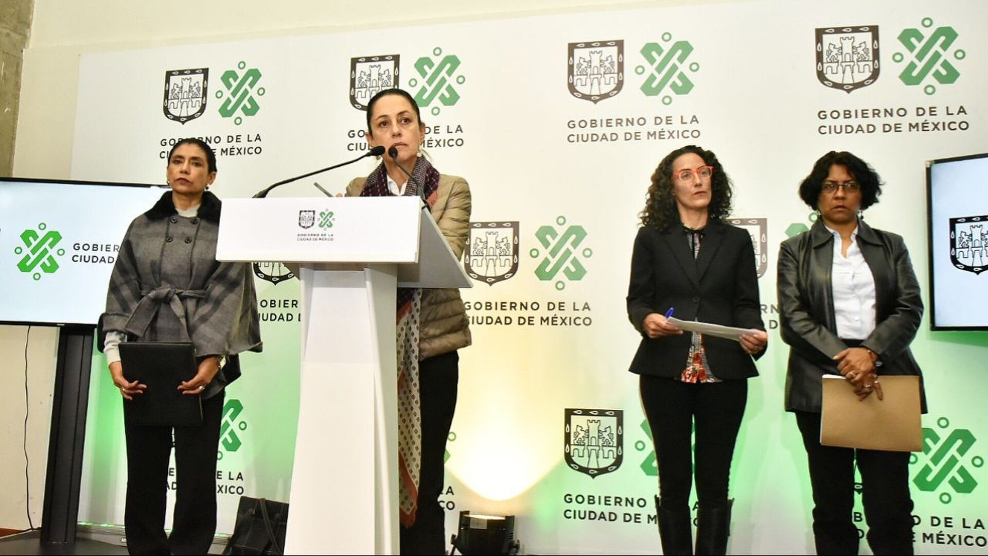 Four women standing at a podium with a city government backdrop.