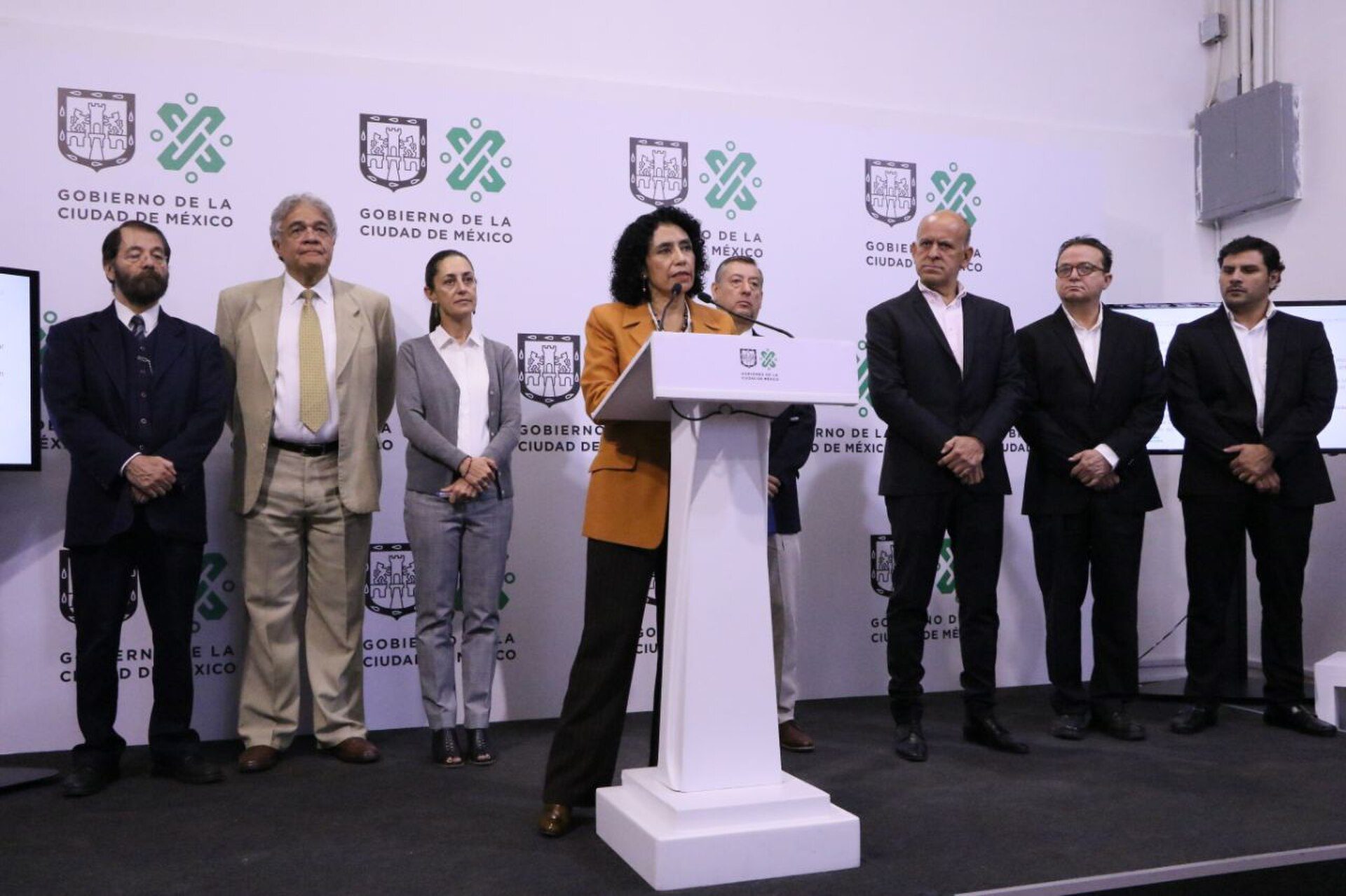 A group of people standing in front of a podium with a backdrop featuring logos.