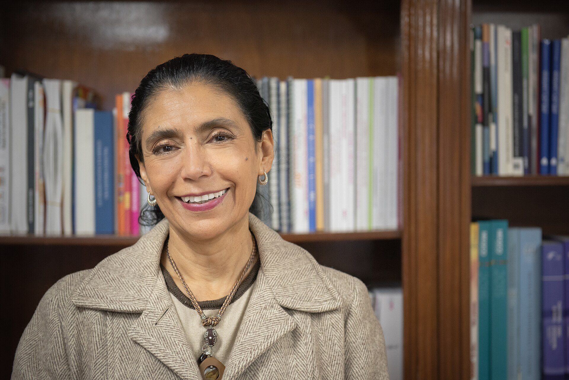 A woman smiles in front of a bookshelf filled with books.
