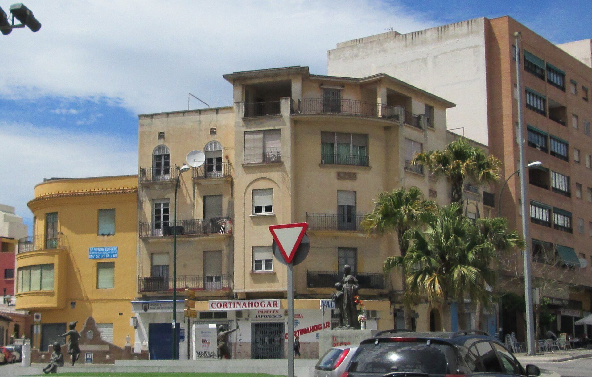A city street scene with a mix of residential buildings, palm trees, and a clear blue sky.