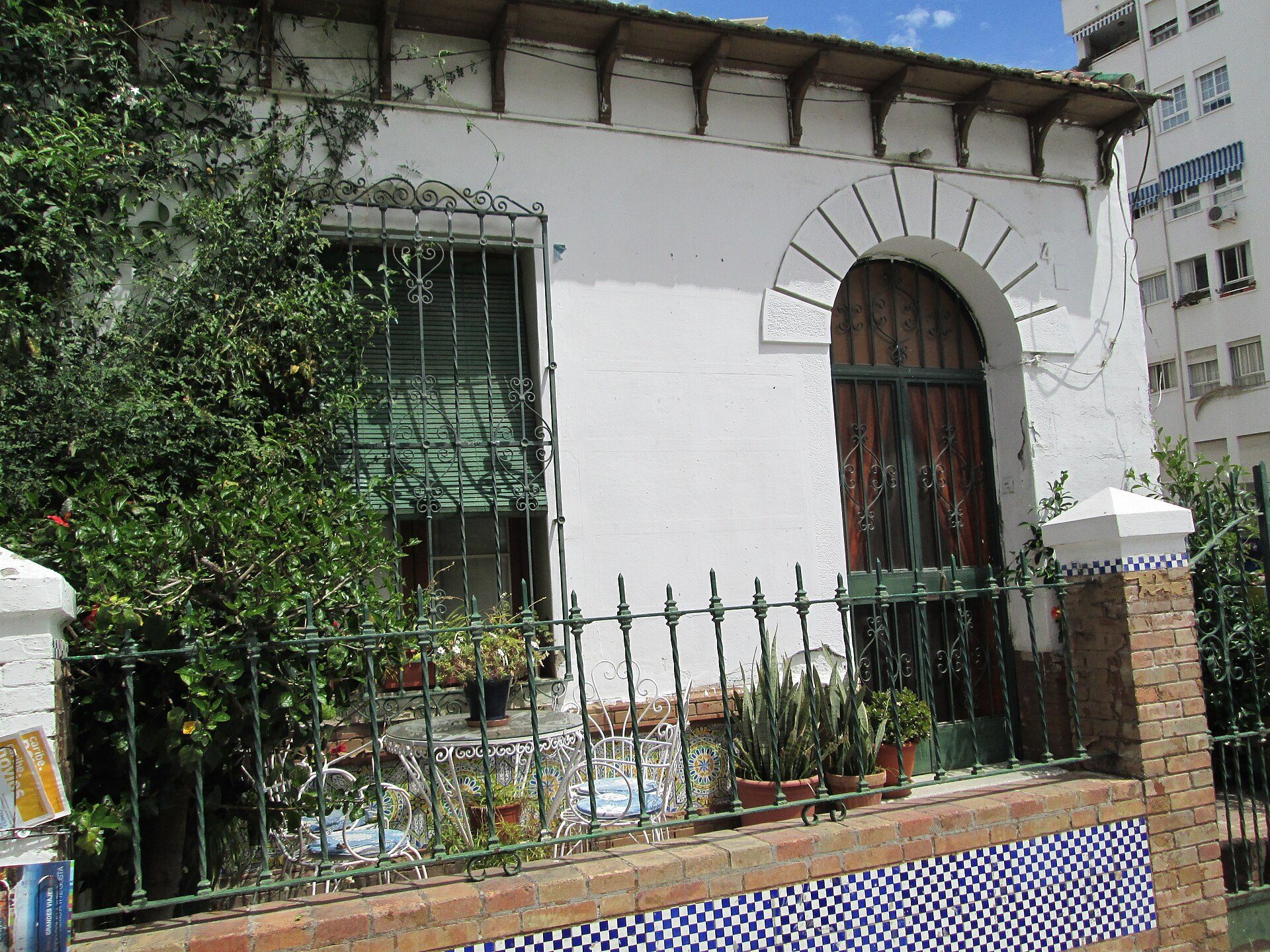 A cozy courtyard with a white-walled room, arched door, and greenery.