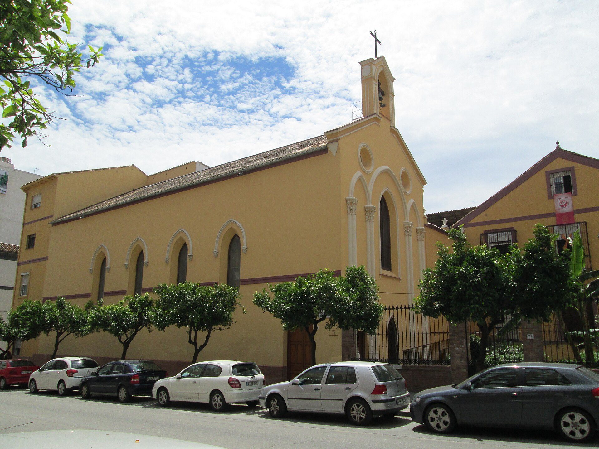 Yellow church with arched windows, parked cars, and green trees.