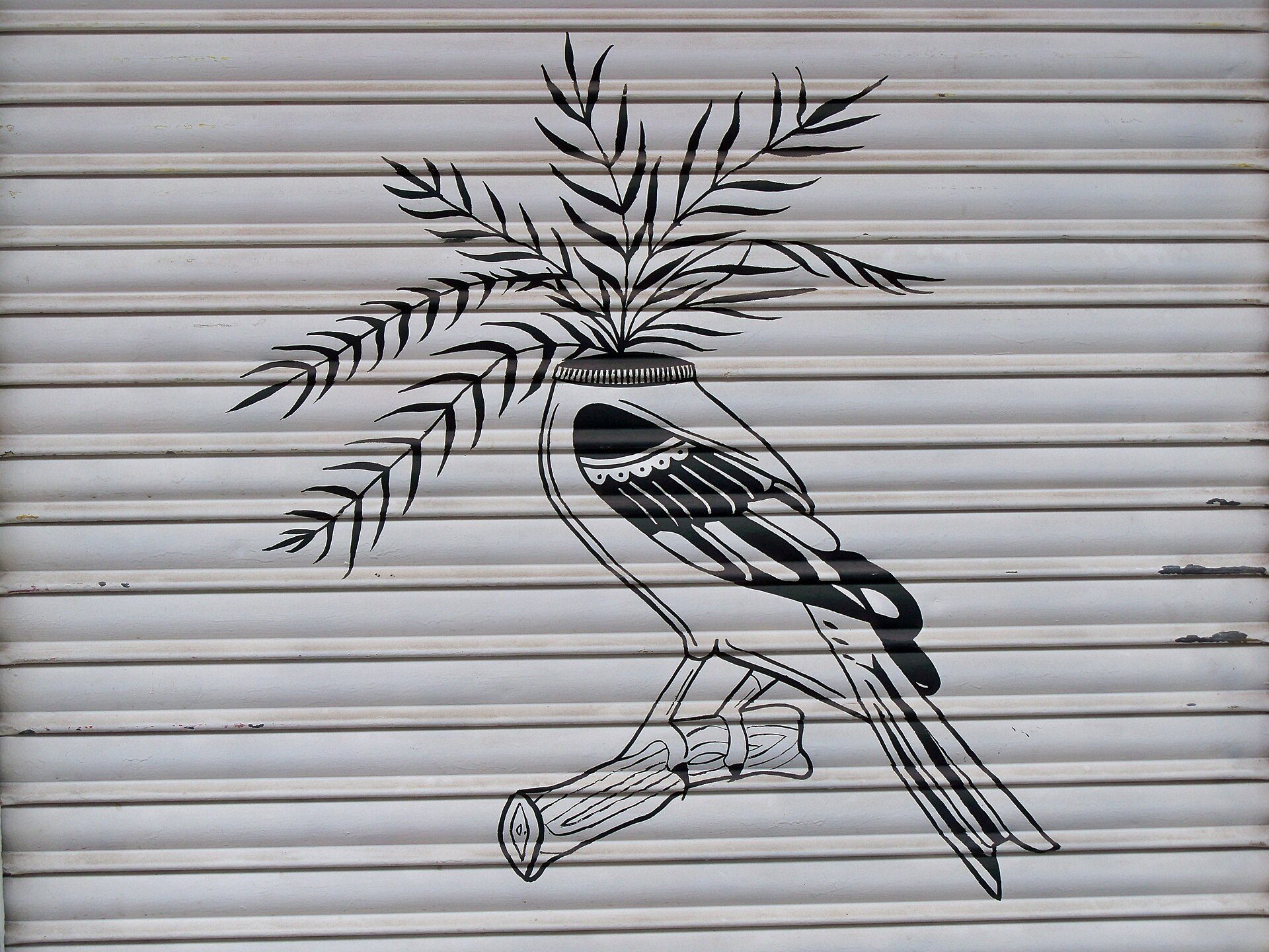A black and white mural of a bird with foliage on a metal shutter.