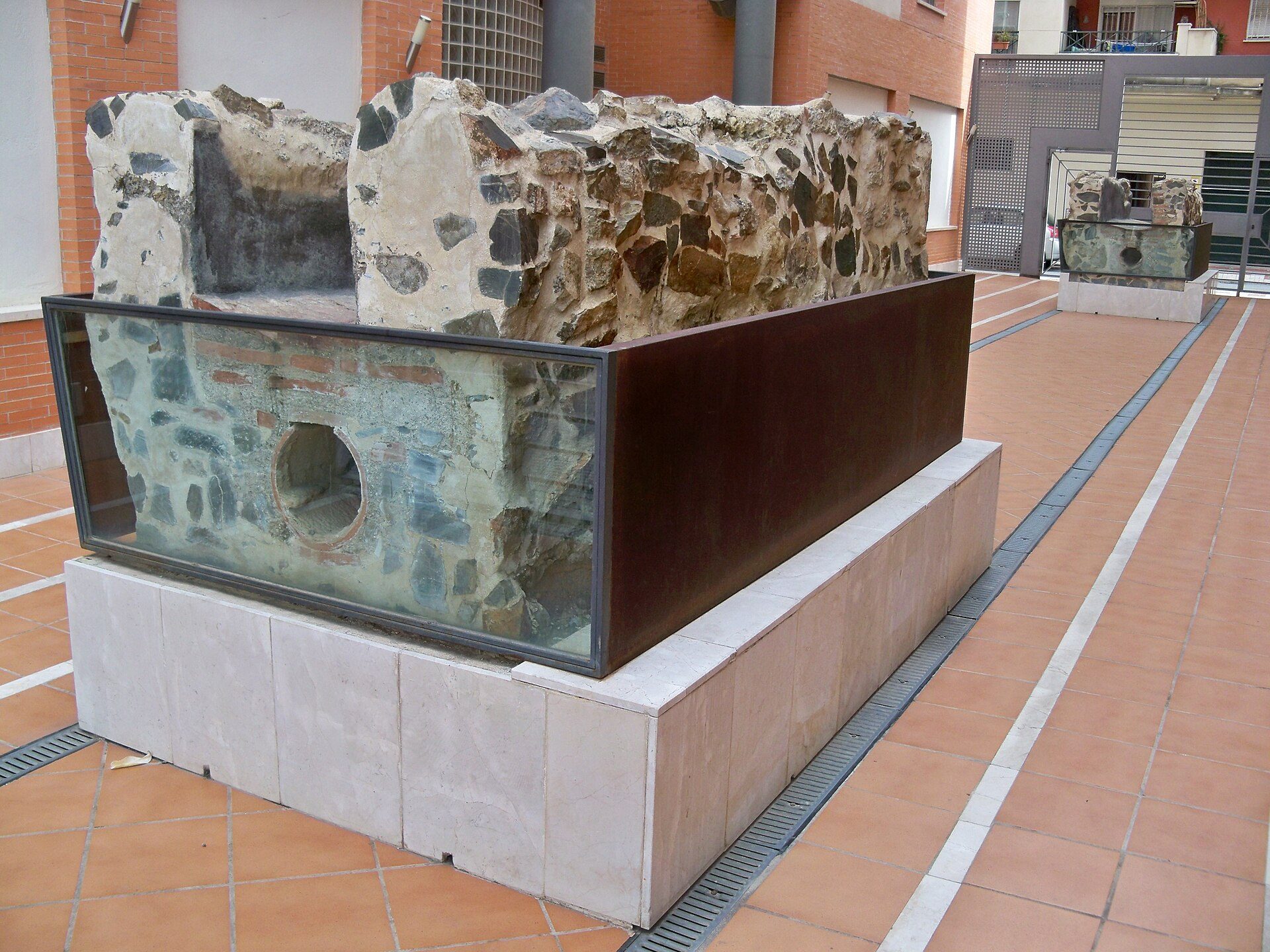 Alt text: Outdoor archaeological exhibit with stone ruins and glass enclosure.