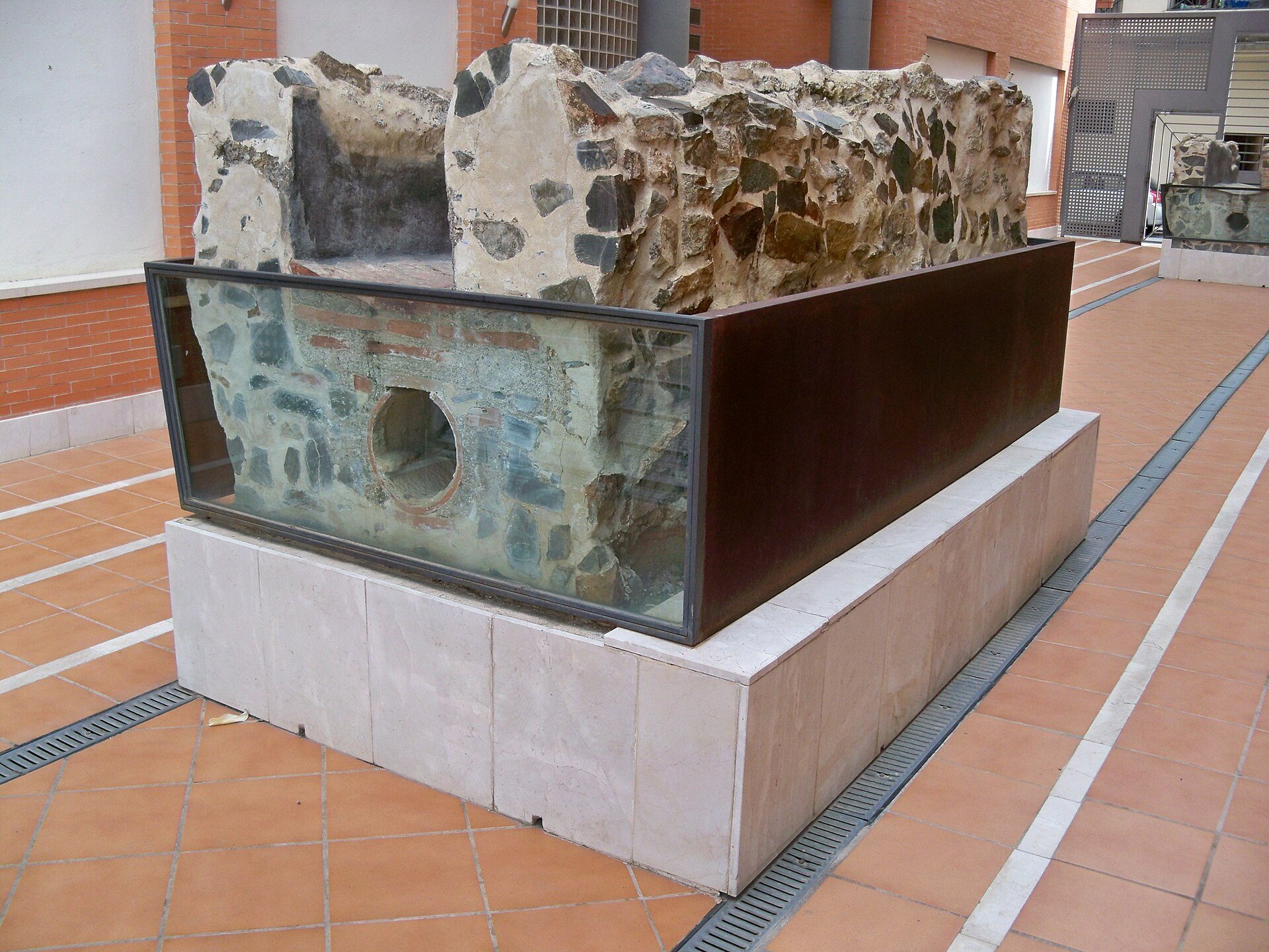 Alt text: Outdoor stone and glass structure with a circular opening, on a tiled patio.