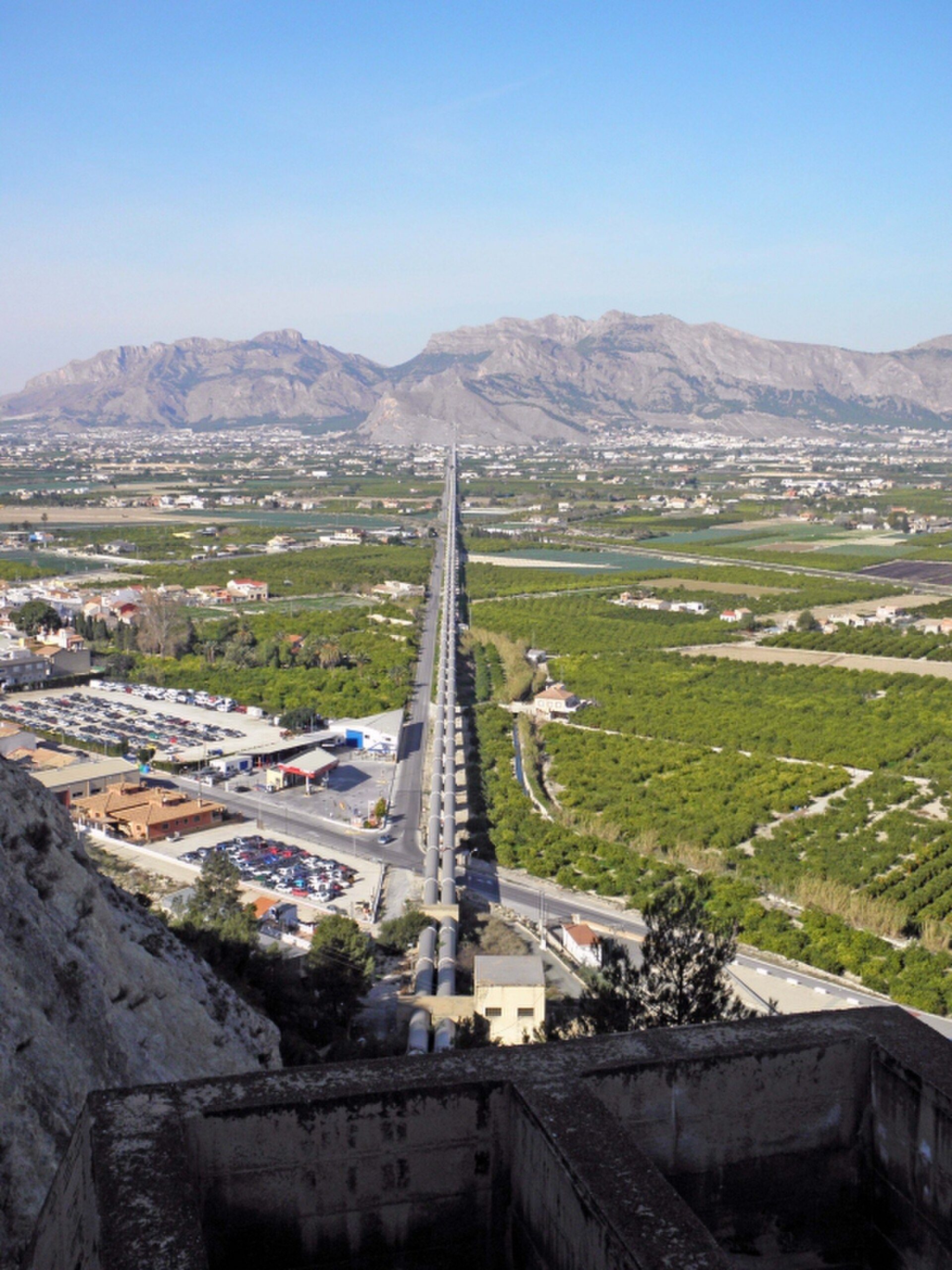 Alt text: Panoramic view of a highway, mountains, and green fields from a room with large windows.