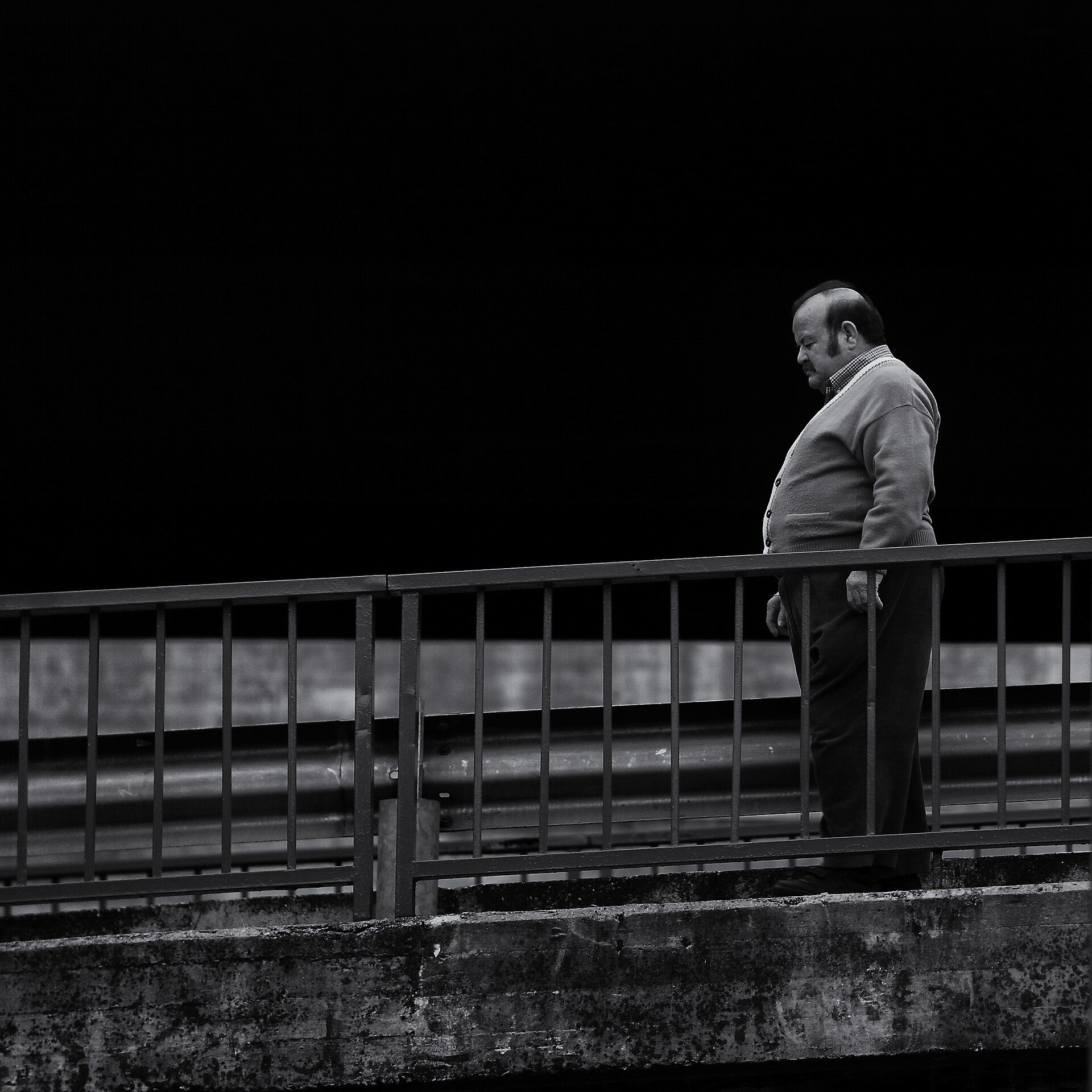 A man stands on a bridge at night, overlooking a dark body of water.