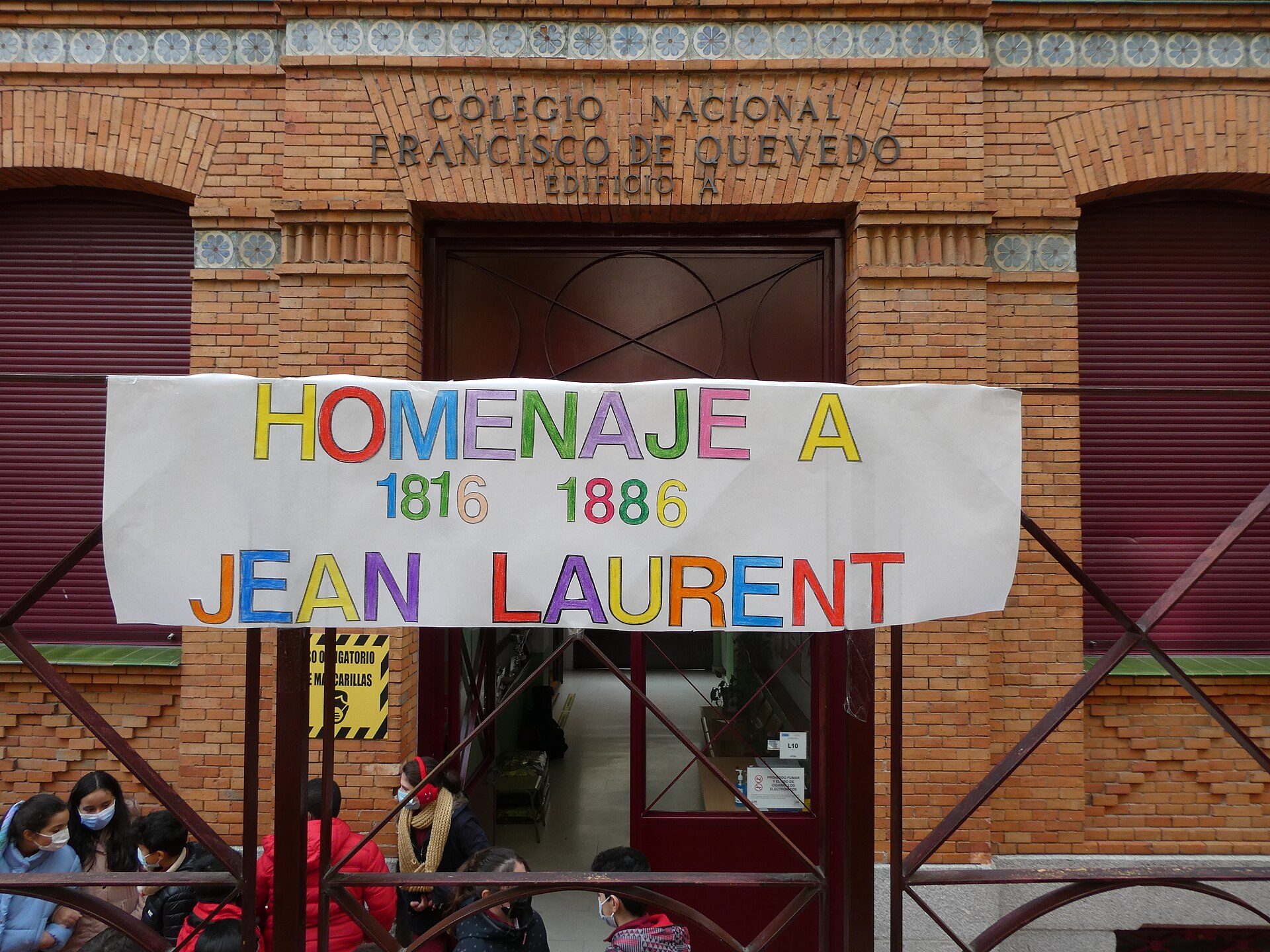 Alt text: Colorful banner in front of a brick building entrance with people gathered.