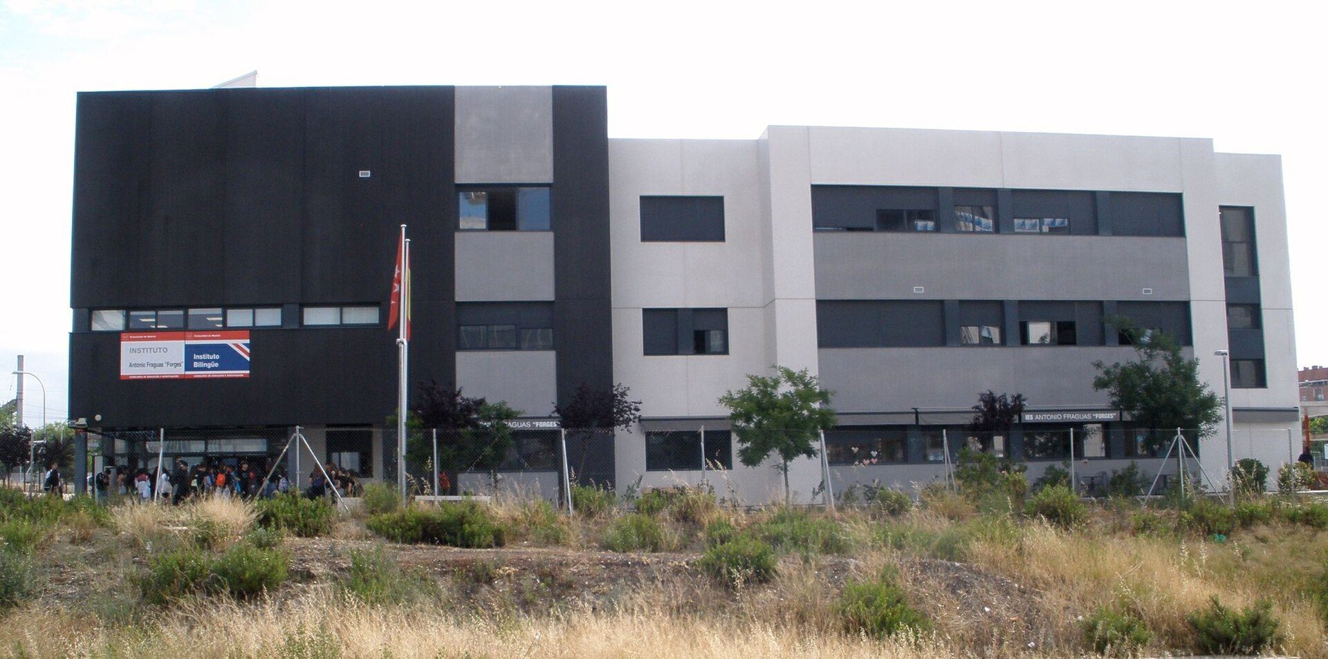 Modern building with large windows, flat roof, and a group of people outside.