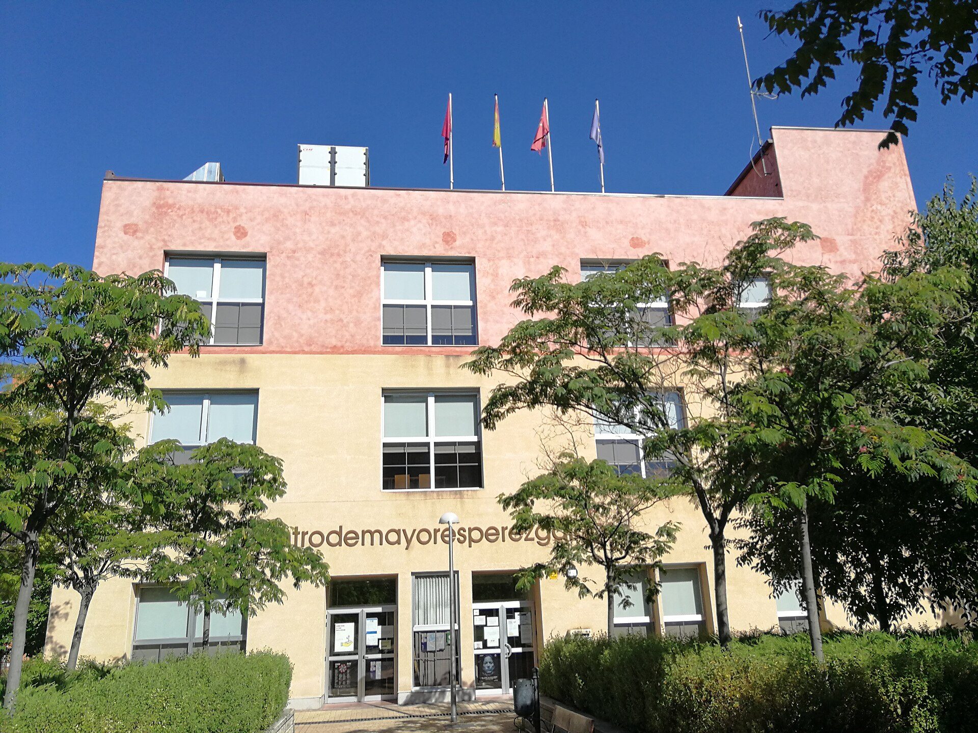 A pink and beige building with flags, surrounded by trees, and a clear blue sky.