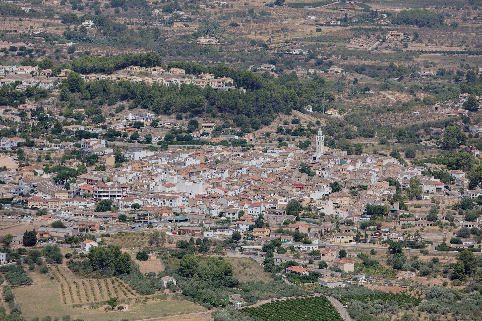 Aerial view of a quaint village with terracotta roofs, lush greenery, and distant hills.