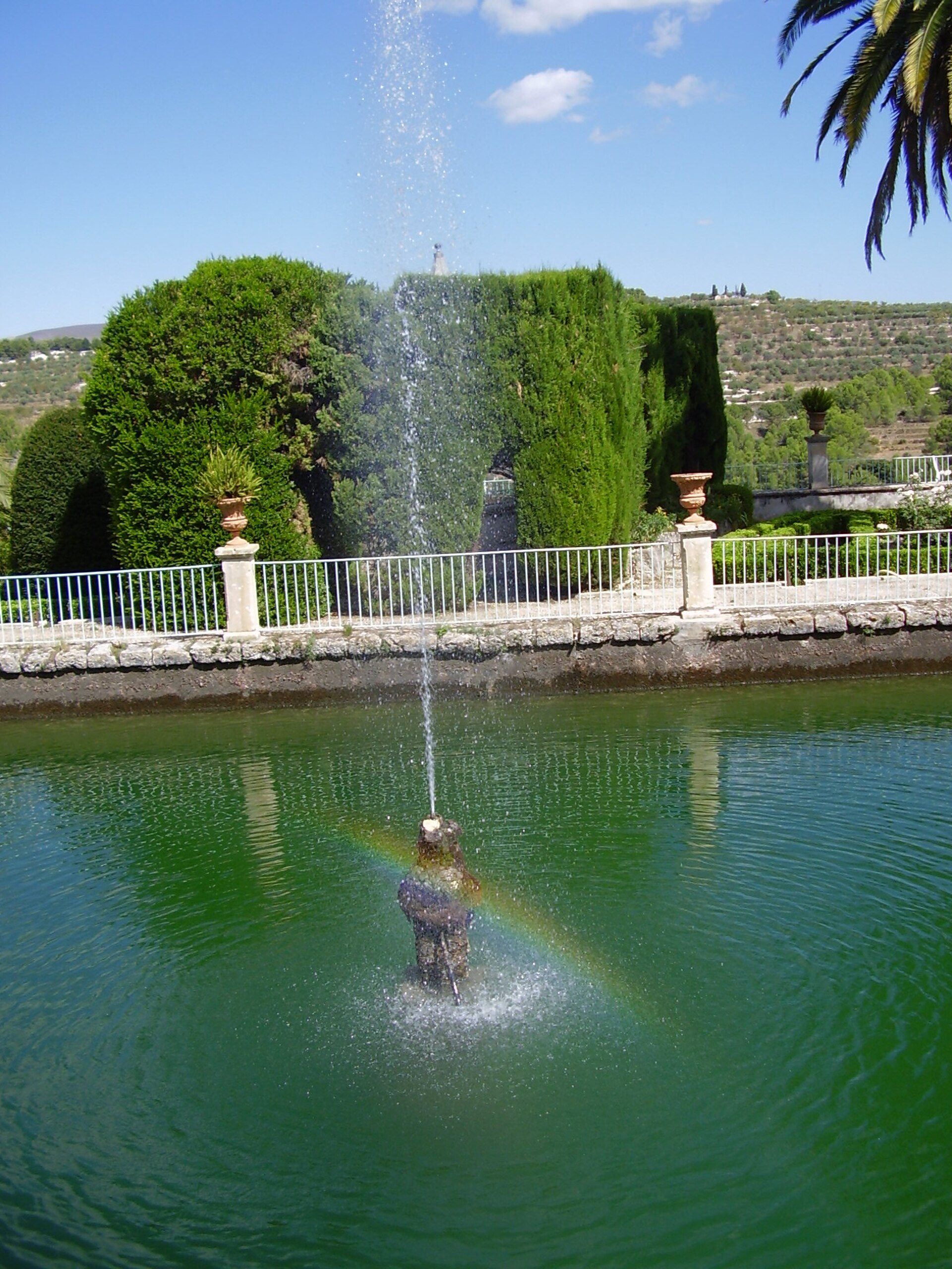 Alt text: Outdoor fountain with greenery and clear blue sky view.