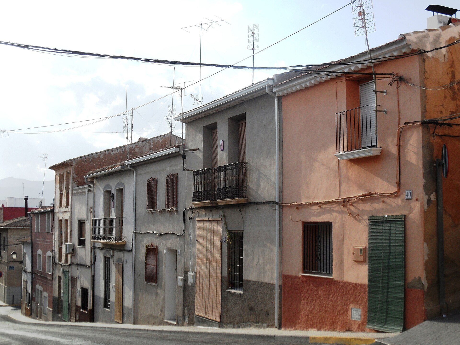 A row of multi-story buildings with balconies, featuring various window styles and satellite dishes.