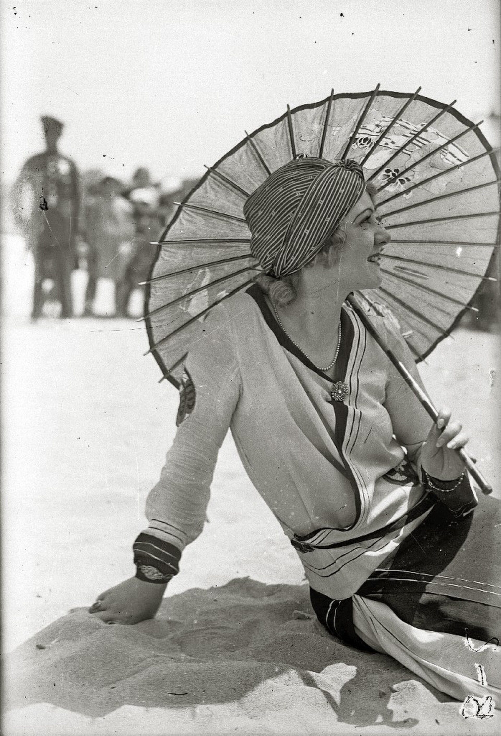 A vintage beach scene with a woman in a striped hat and dress, holding a parasol.