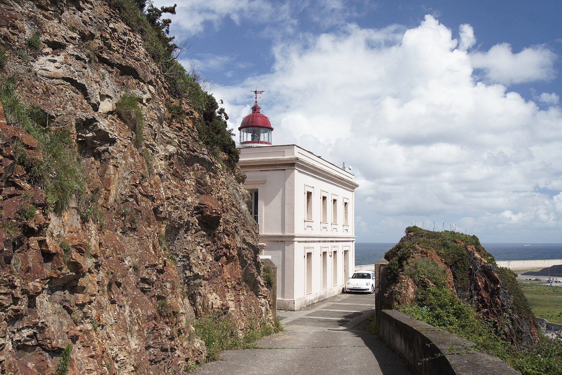 Cozy room with ocean view, featuring a red-roofed lighthouse and rocky cliffside.