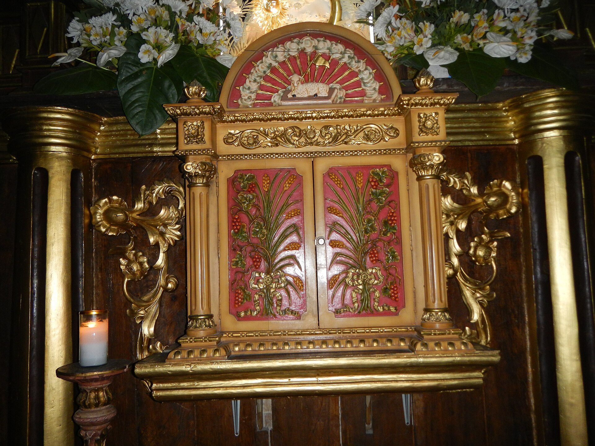 Alt text: Ornate altar with floral decorations, candles, and intricate carvings in a church setting.