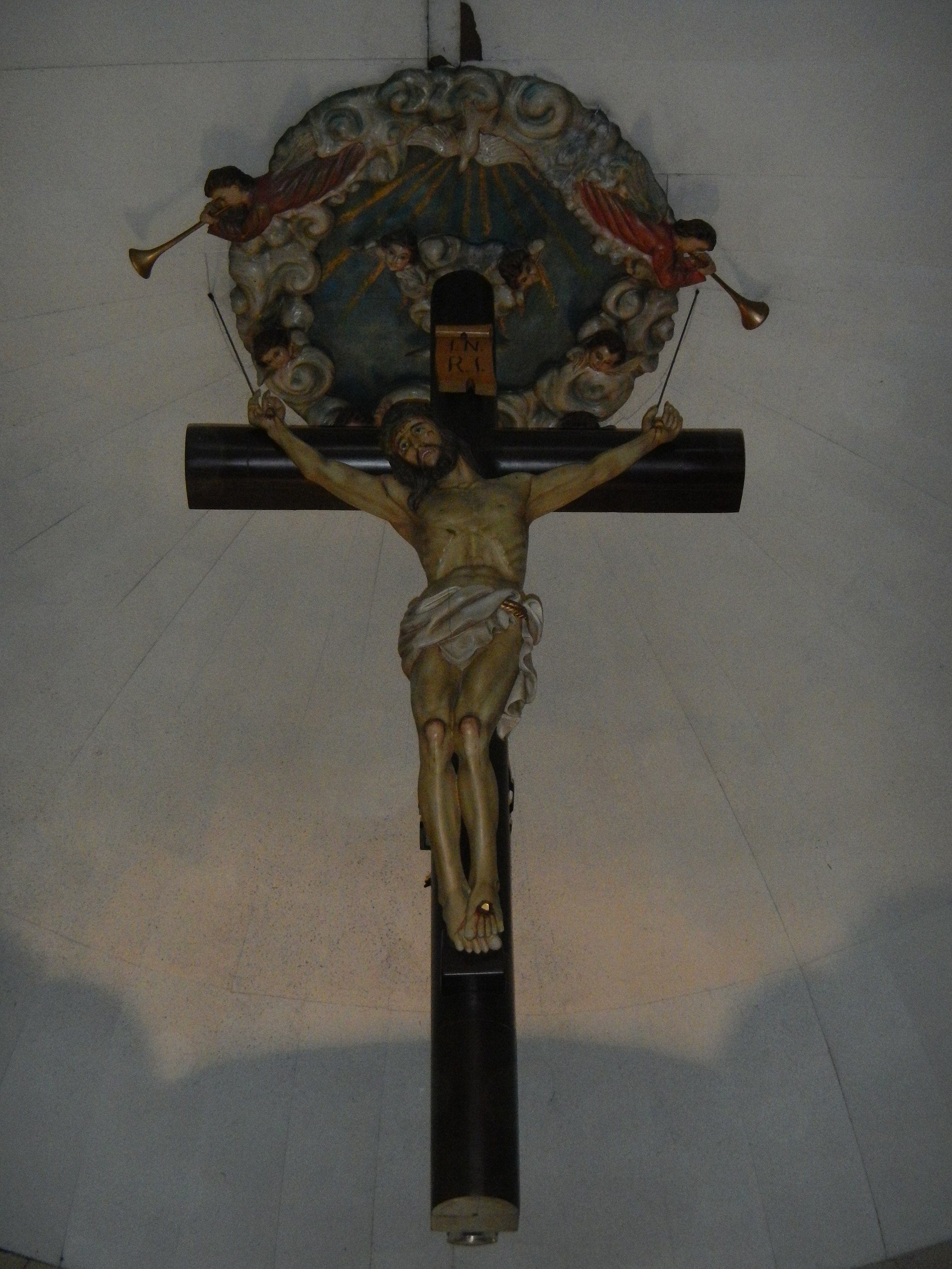 Alt text: A crucifix with a detailed depiction of Jesus on a cross, set against a white wall.