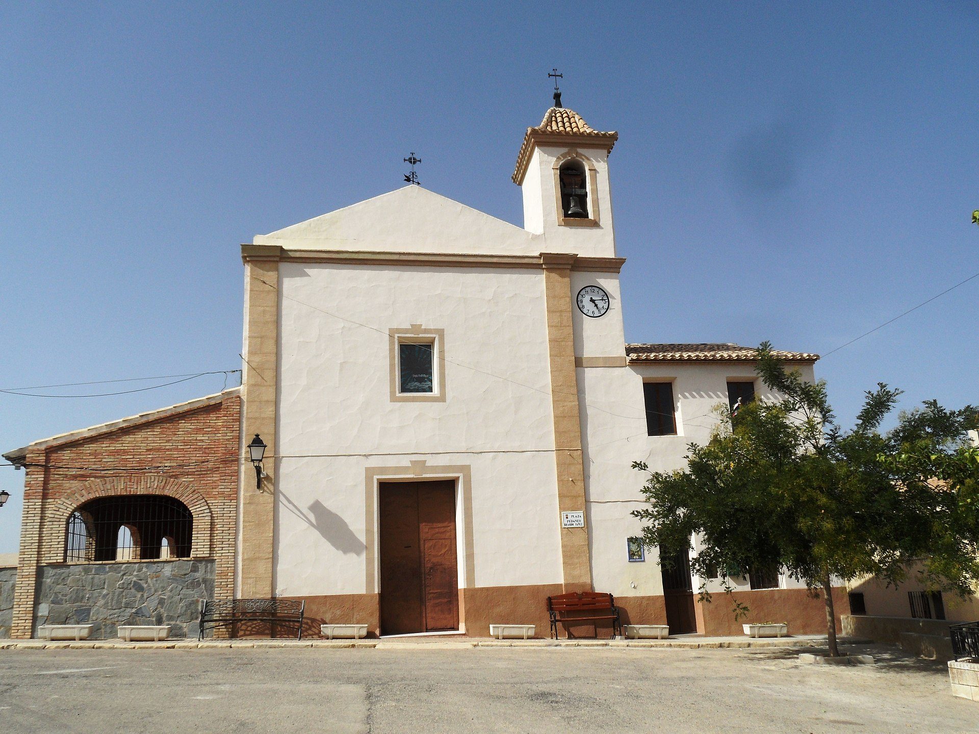 A small church with a bell tower, white facade, and a clear blue sky view.