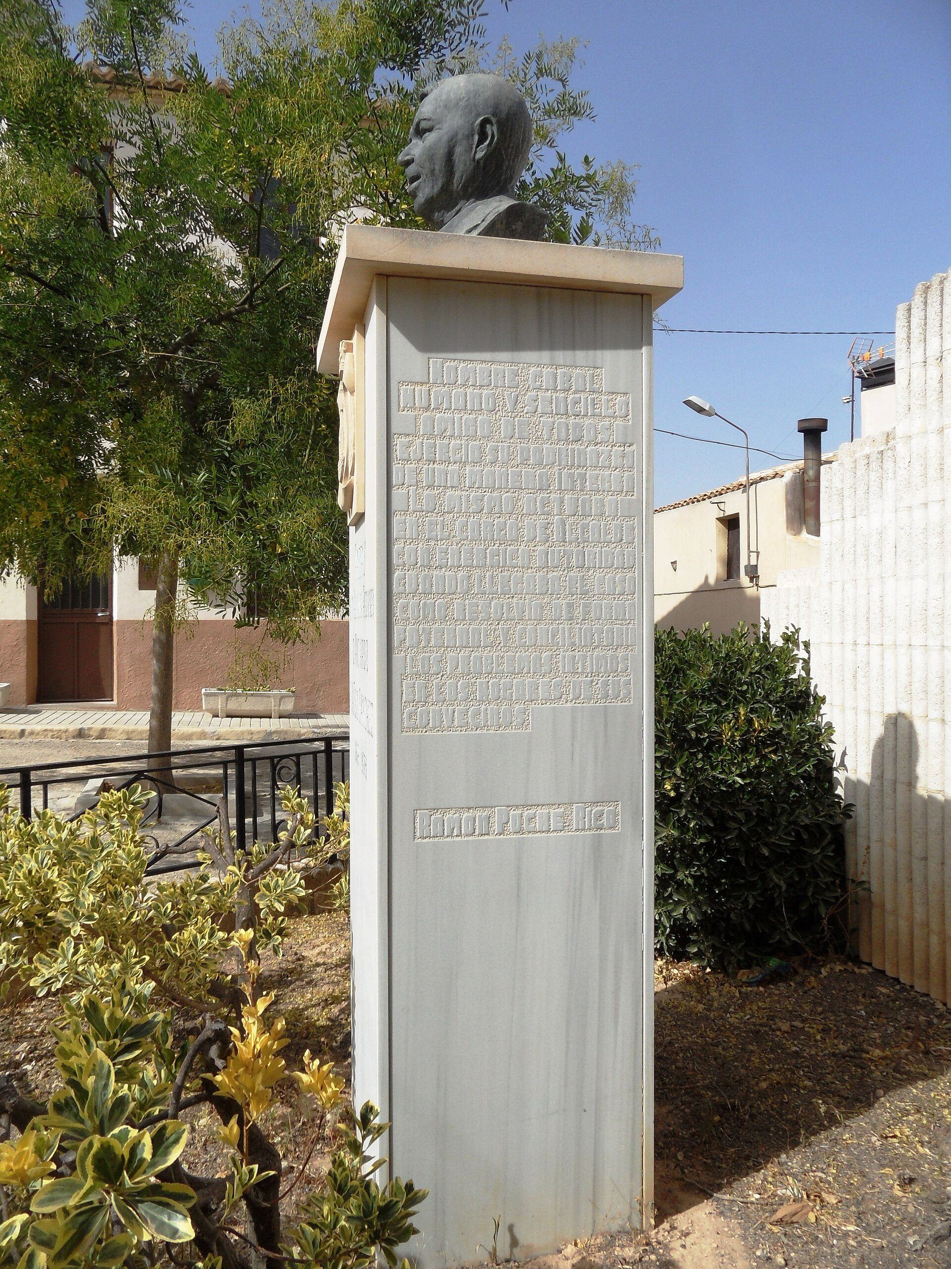 Alt text: Outdoor bust statue with plaque, surrounded by greenery and trees.