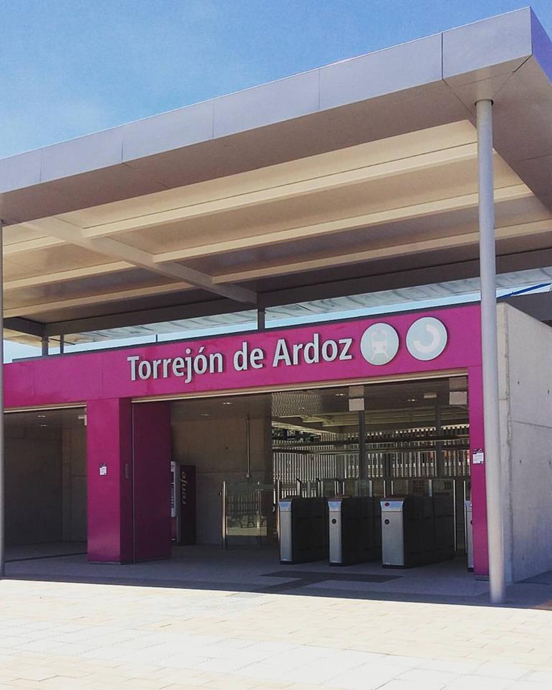 Alt text: Modern entrance to Torrejón de Ardoz with pink and white color scheme, featuring turnstiles and a clear sky view.