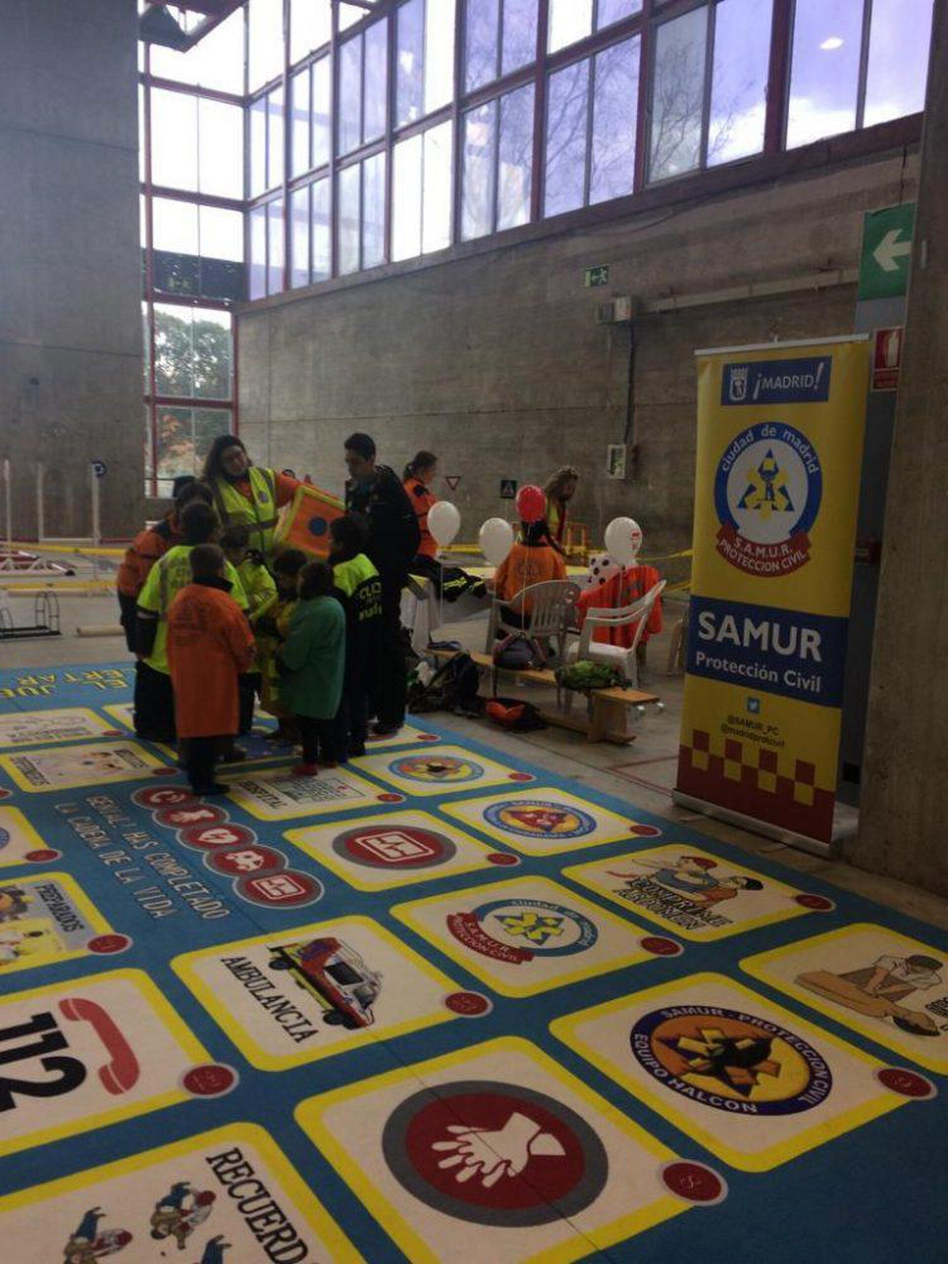 Indoor event space with large windows, colorful floor markings, and informational banners.