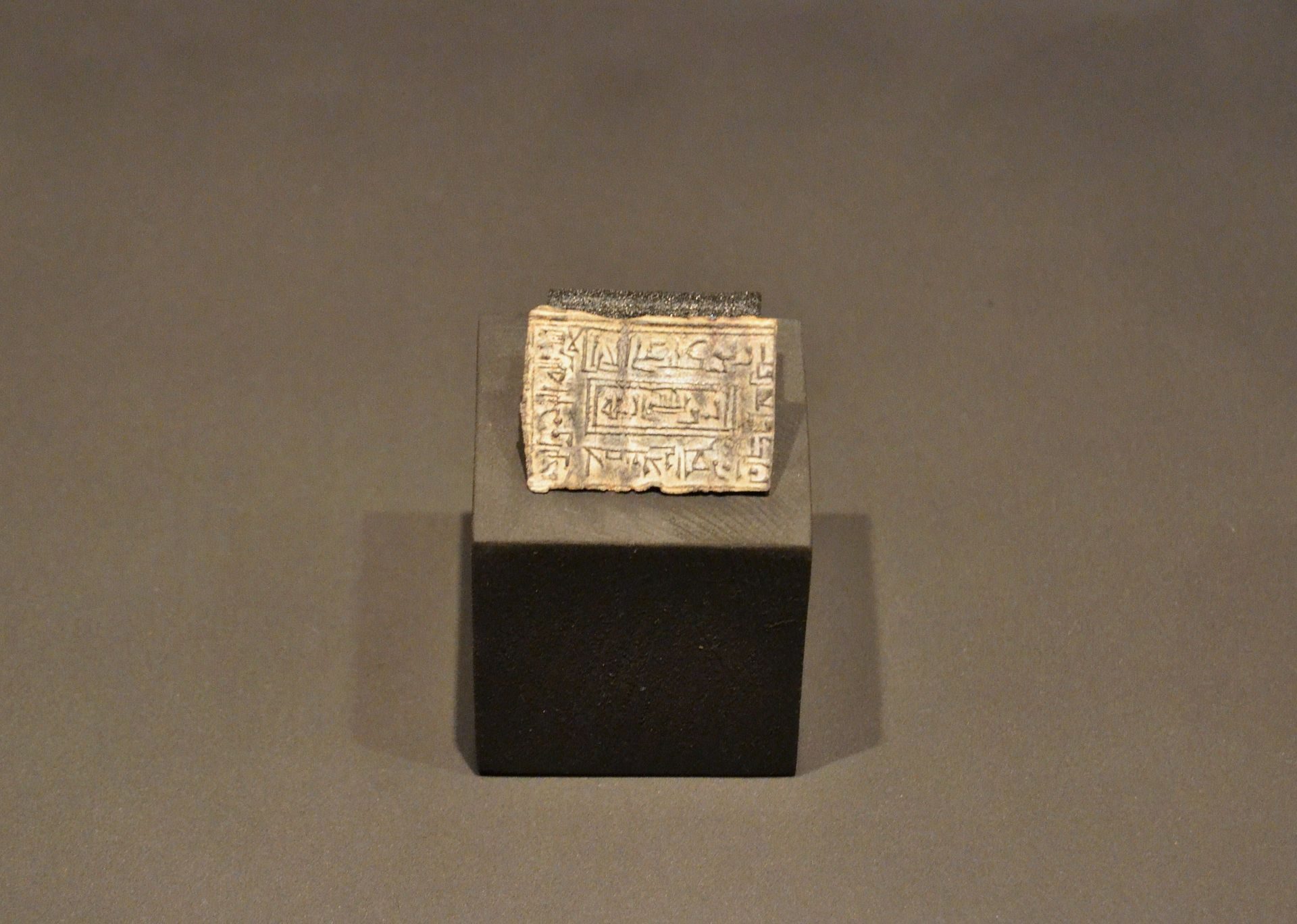 Small, intricately carved stone cube on a black pedestal.