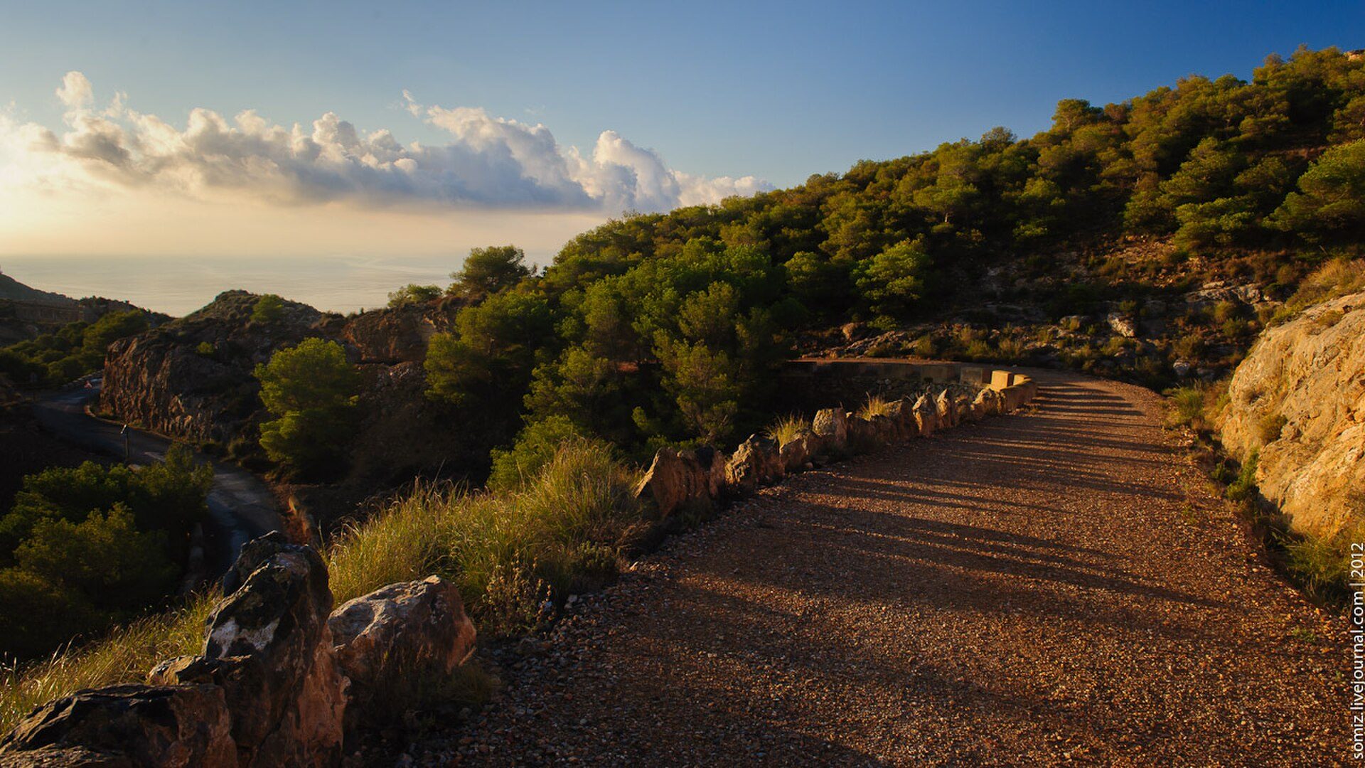 A scenic mountain road with lush greenery and a clear blue sky.