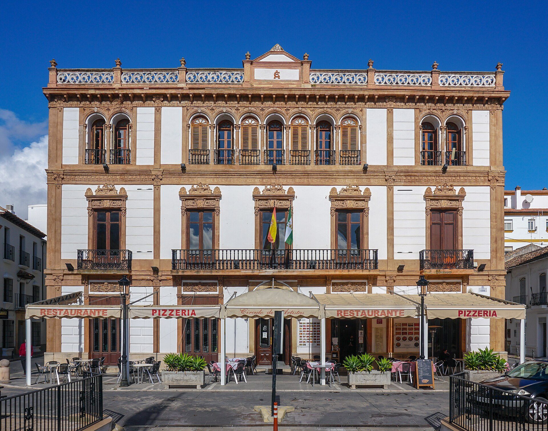 A three-story building with a restaurant on the ground floor, featuring balconies and a clear blue sky view.