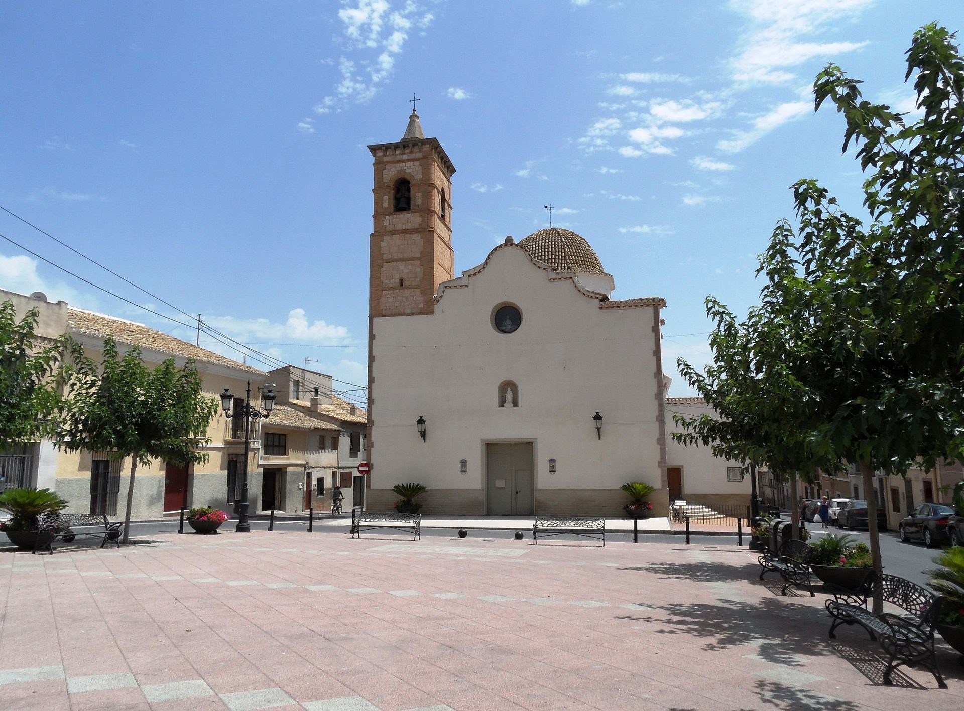 Alt text: Historic church with bell tower, surrounded by trees and benches in a quaint town square.