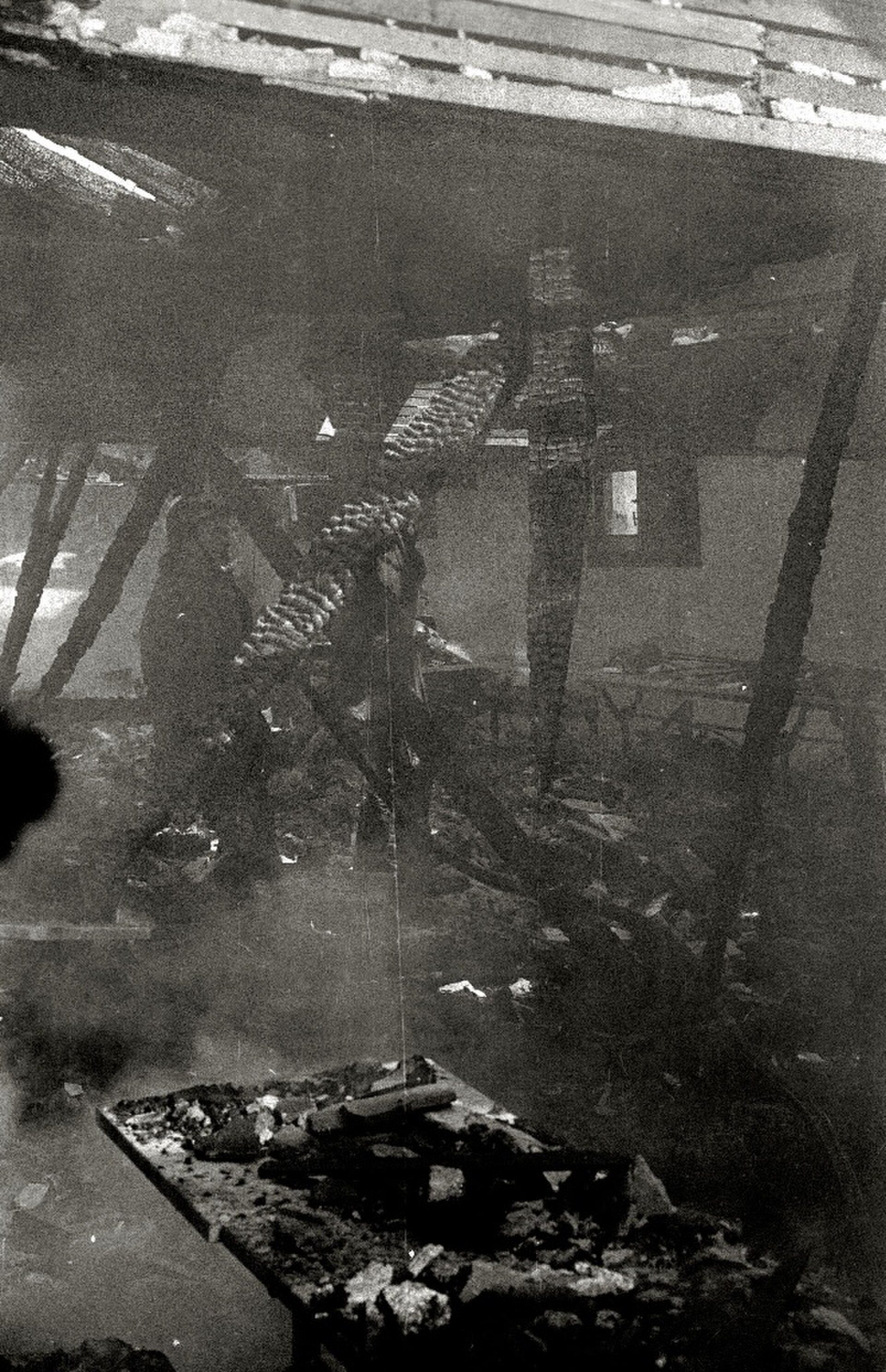 Black and white photo of a damaged room with debris and a broken ceiling.