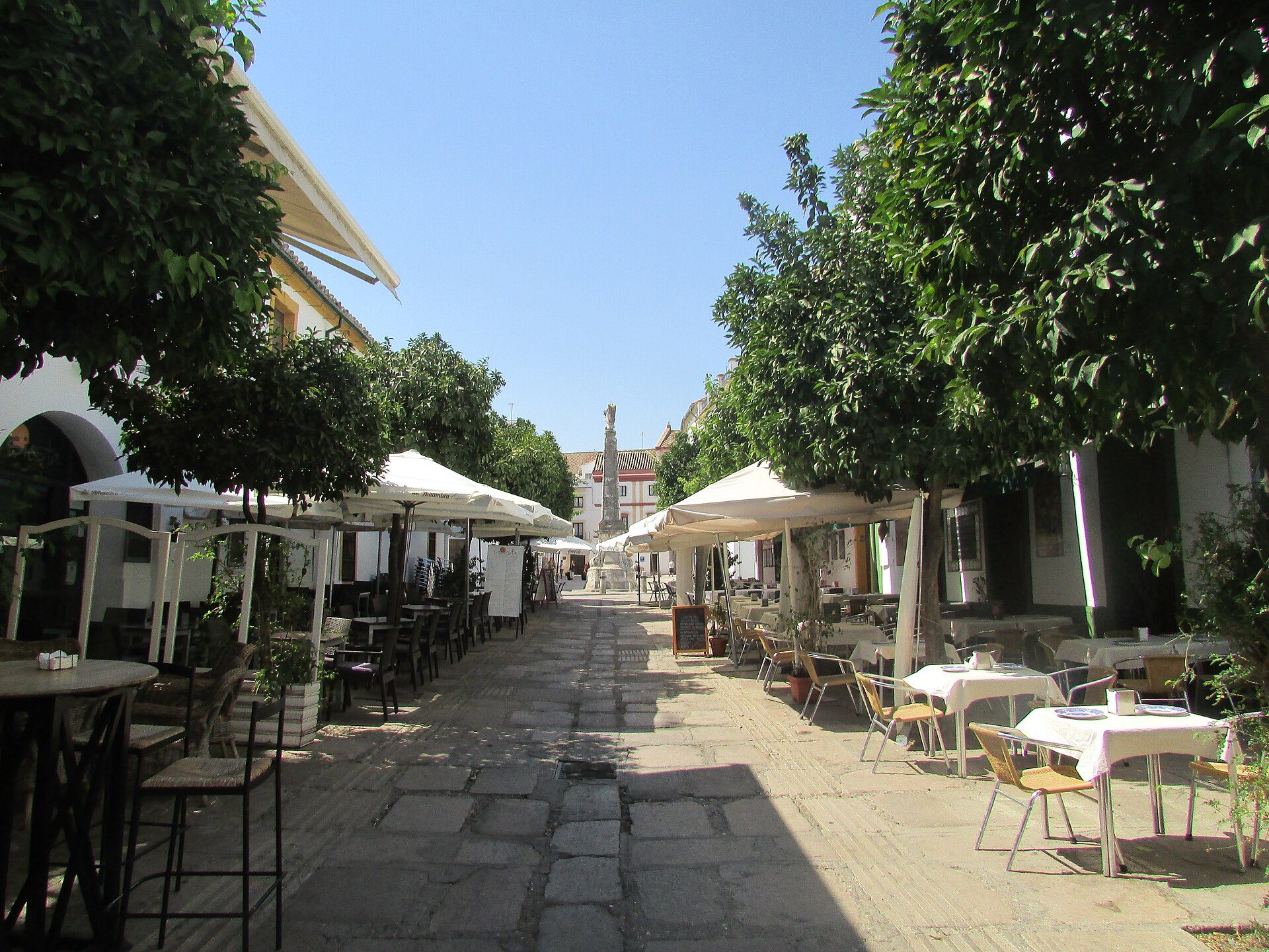 Outdoor dining area with white umbrellas, stone pavement, and lush green trees.
