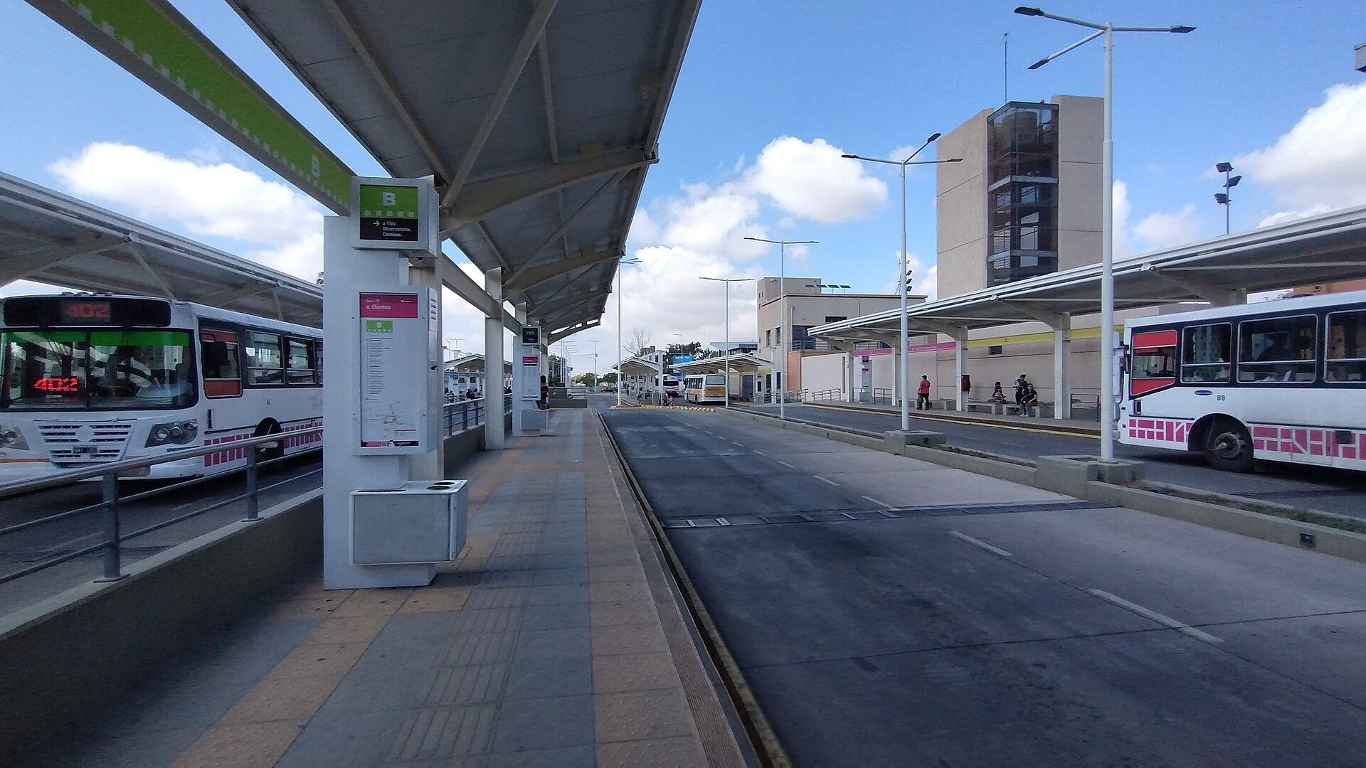 Alt text: Modern bus station with two buses, clear sky, and urban buildings.