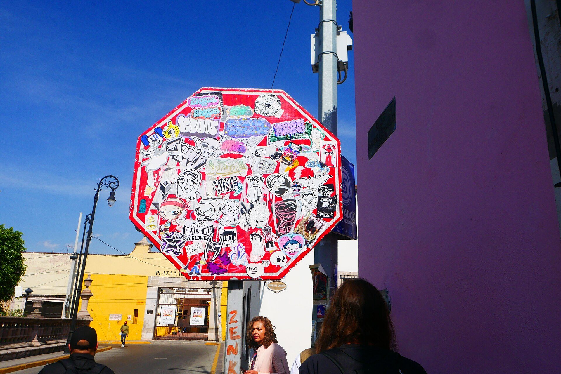 Alt text: Street view with a graffiti-covered stop sign, pedestrians, and colorful buildings.