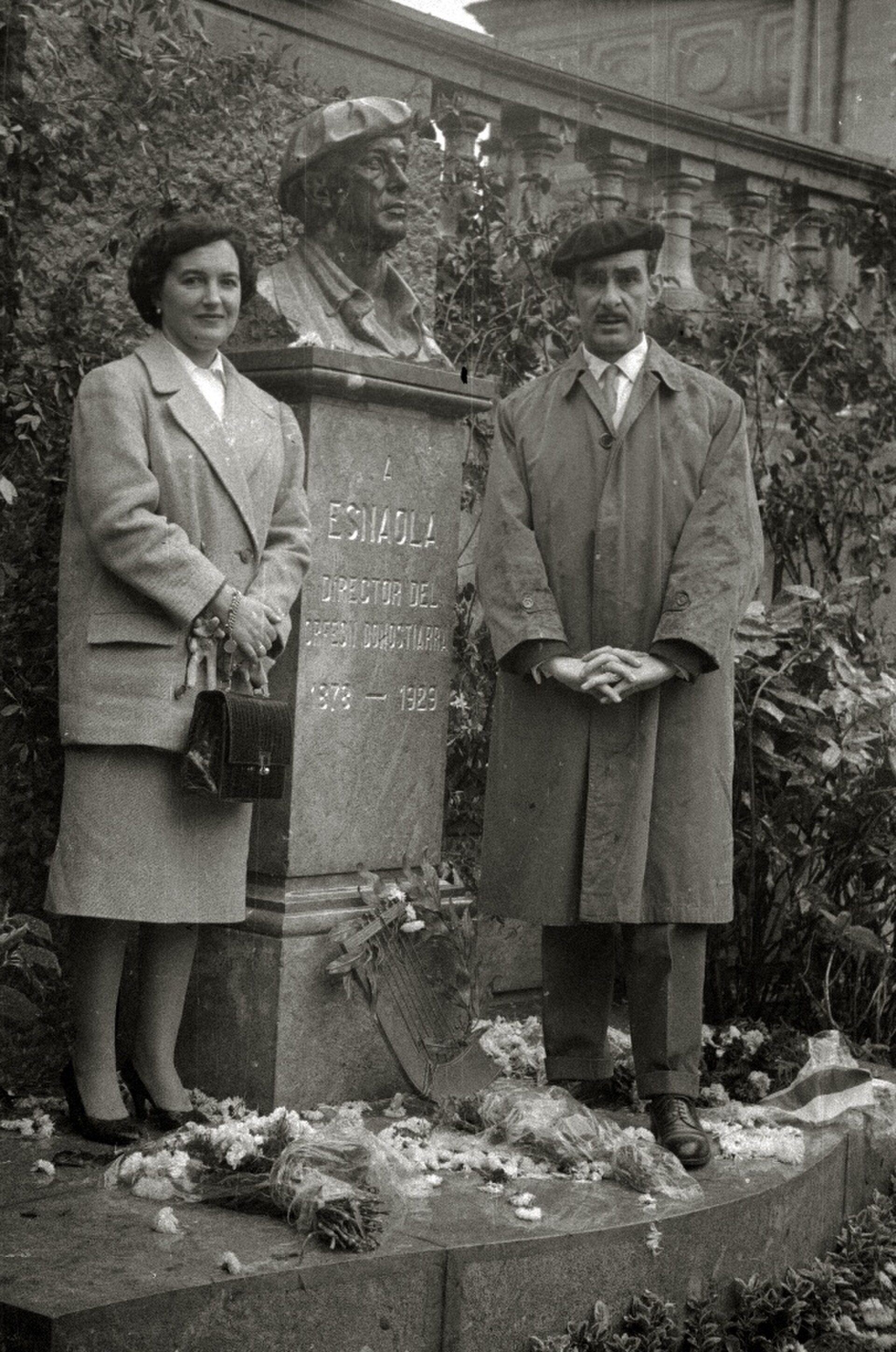 Alt text: Black and white photo of a couple standing in front of a statue with inscriptions.