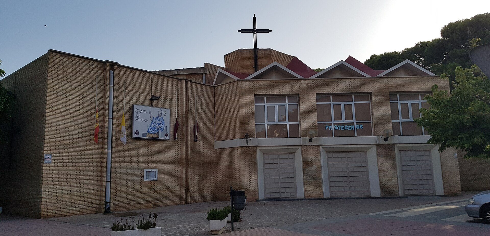 Alt text: Brick building with garage, cross on roof, and sign reading "FLORESTAMOS".