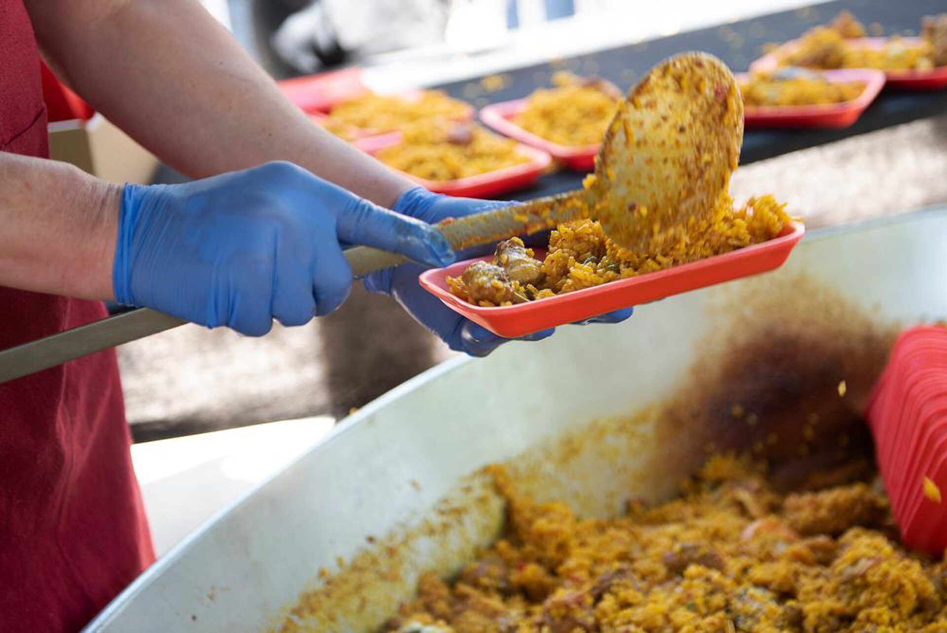 A person in blue gloves serving food from a large pot into a red tray.