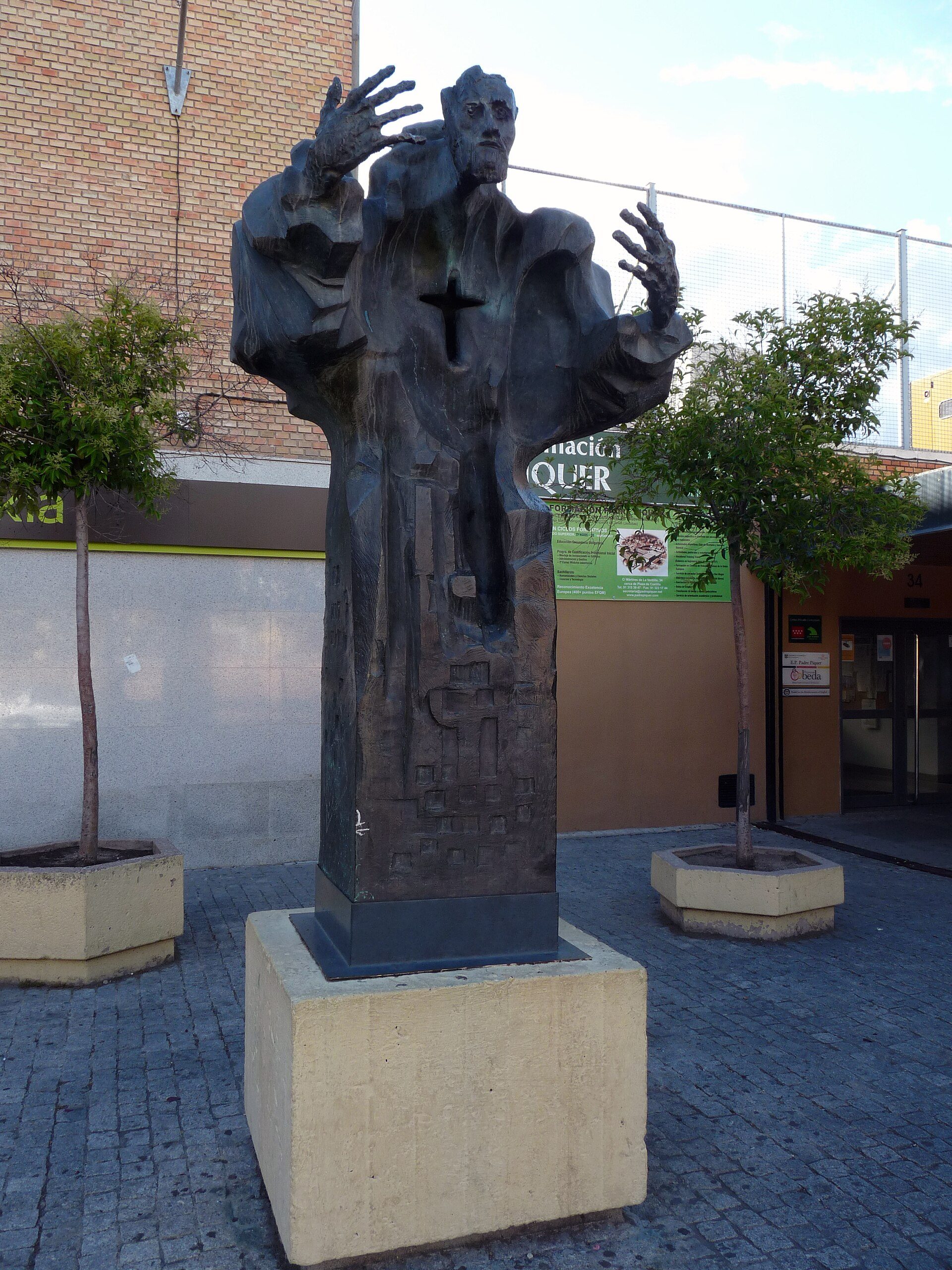 Alt text: Outdoor statue of a robed figure with raised hands, standing on a pedestal.