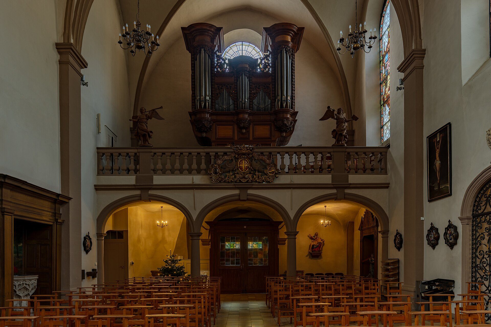 Interior view of a church with wooden pews, an organ, stained glass windows, and statues.