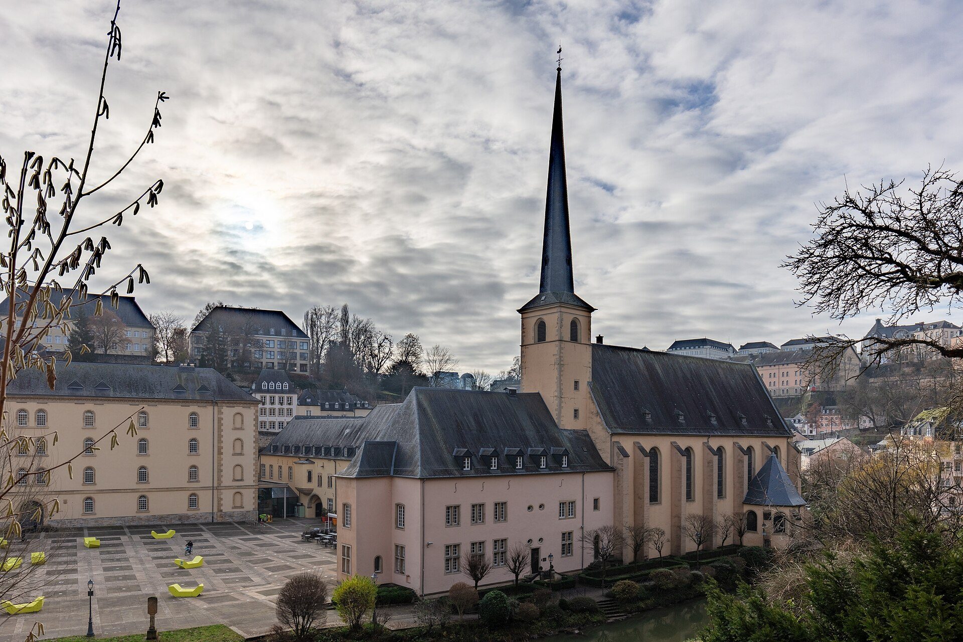 Alt text: "Pink church with tall spire, surrounded by trees and buildings, scenic view.