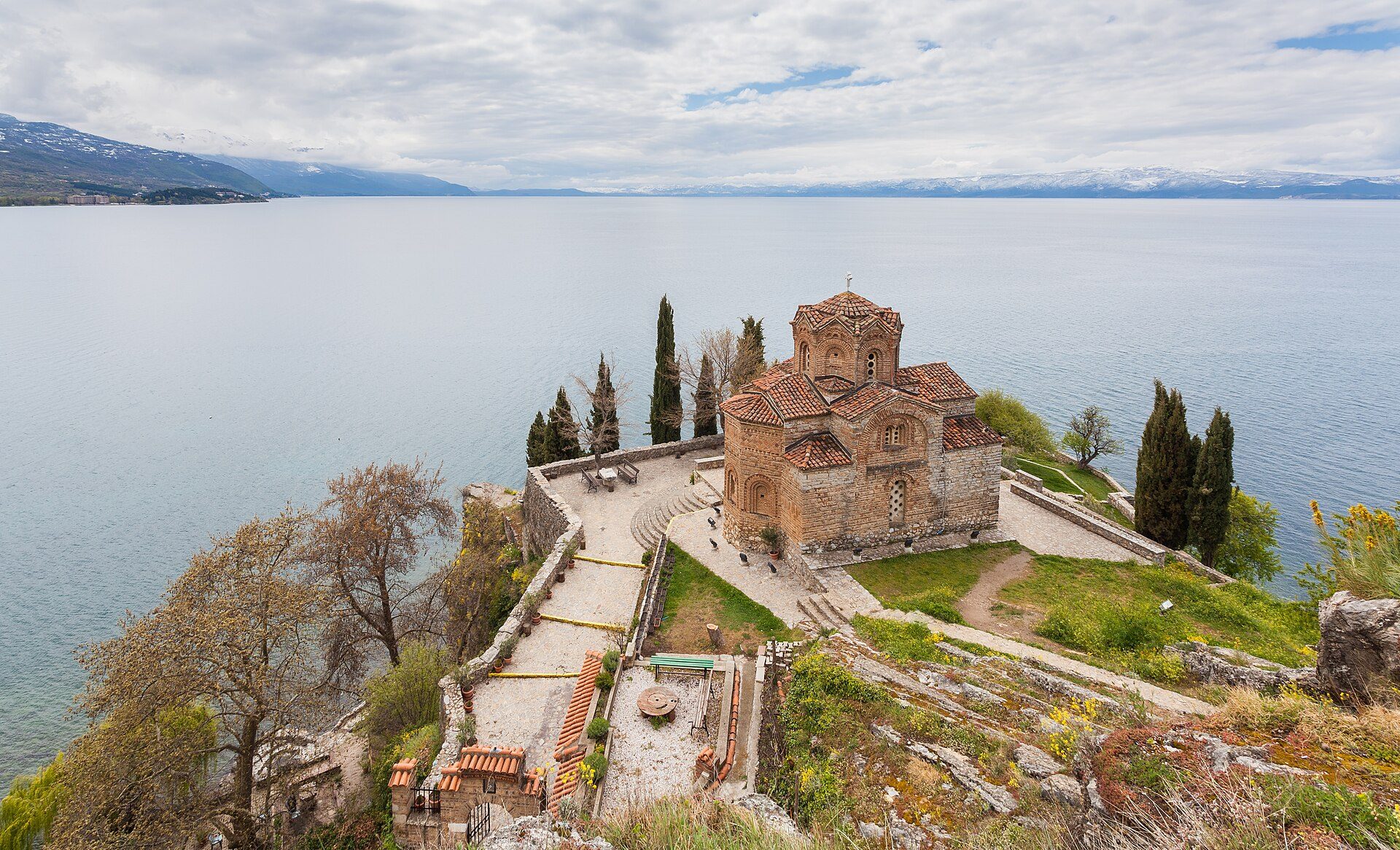 Aerial view of a historic stone church with a lake and mountains in the background.