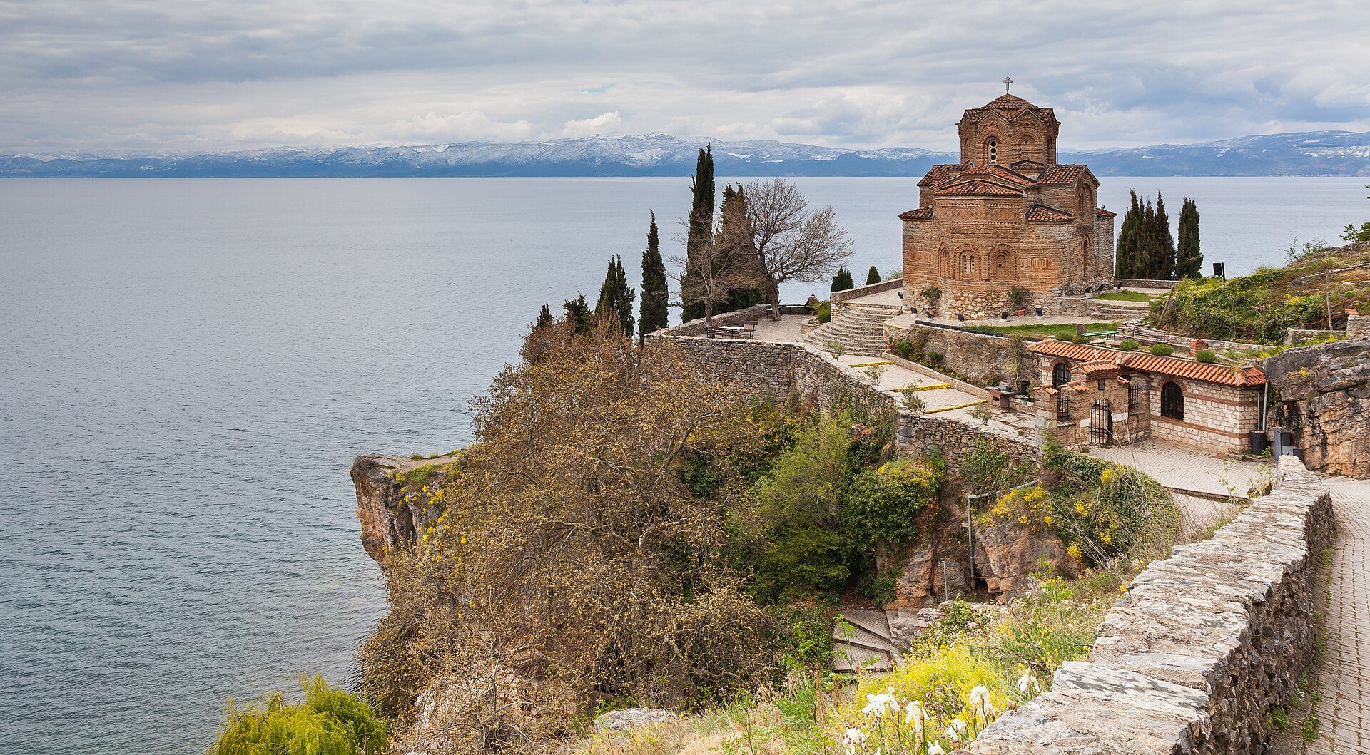 Alt text: Historic stone church with scenic lake and mountain view, surrounded by trees and stone walls.