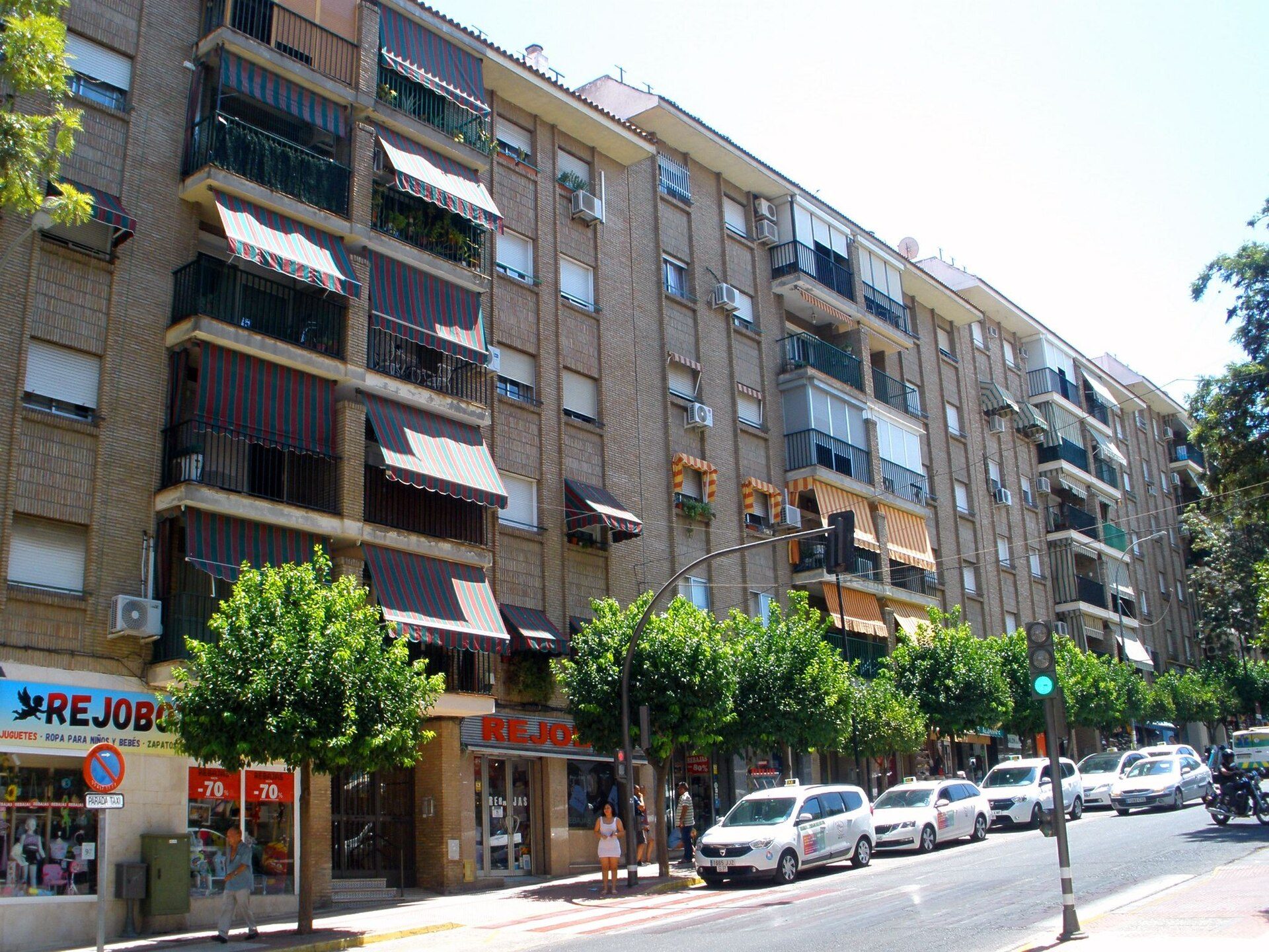 A multi-story apartment building with balconies, green awnings, and street-level shops.